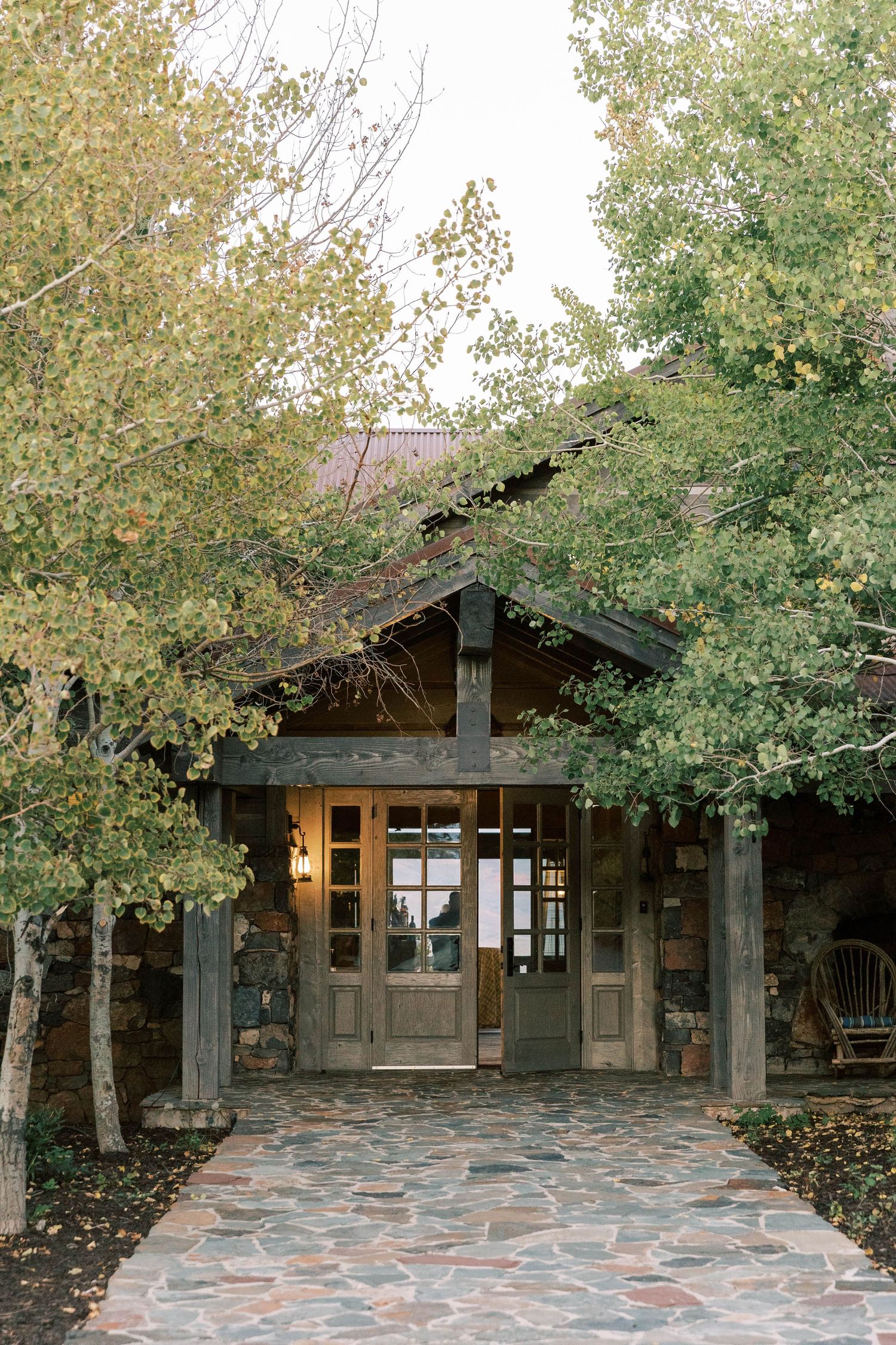 Rustic stone and wood cabin entrance framed by autumn trees with a flagstone path of promontory park city.