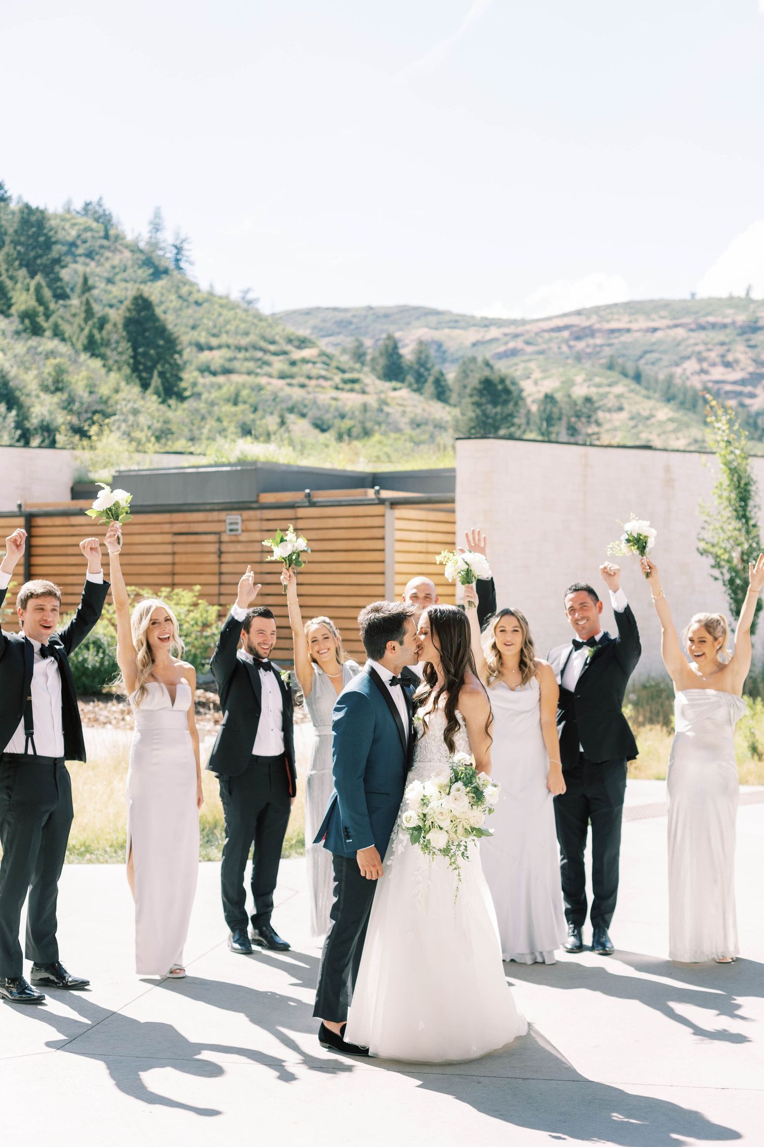 Joyful wedding party celebrating with raised arms in outdoor mountain setting.