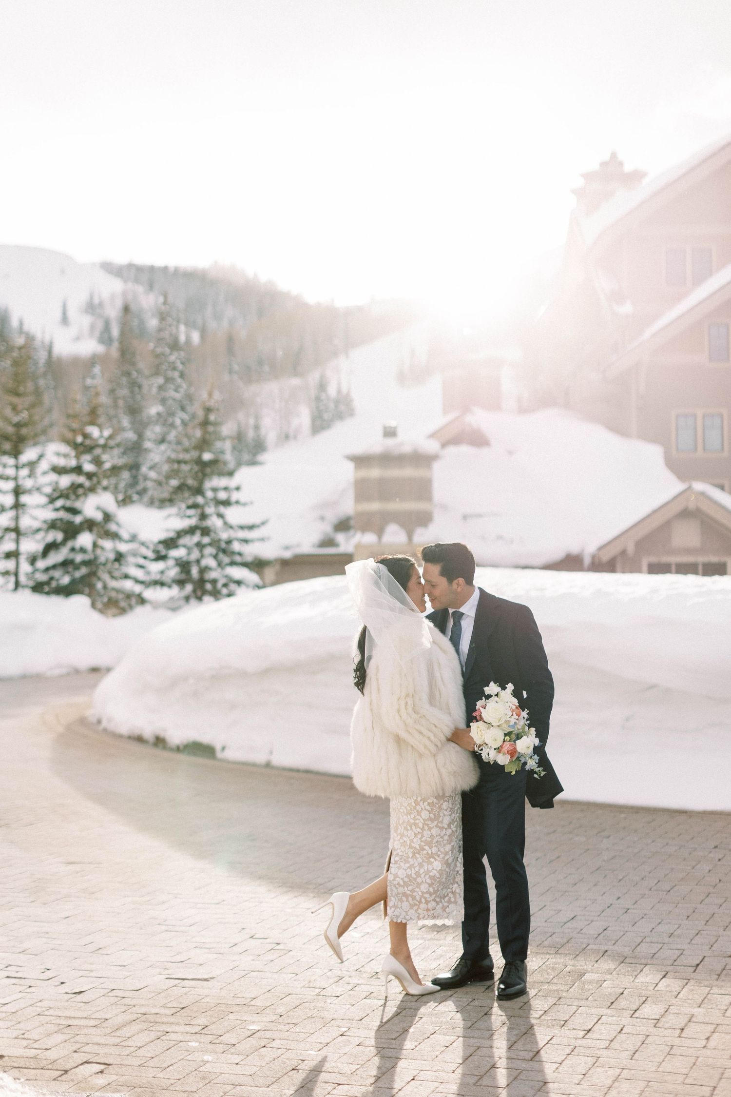 Wedding couple embracing on snowy mountain path with montage deer valley in the background.