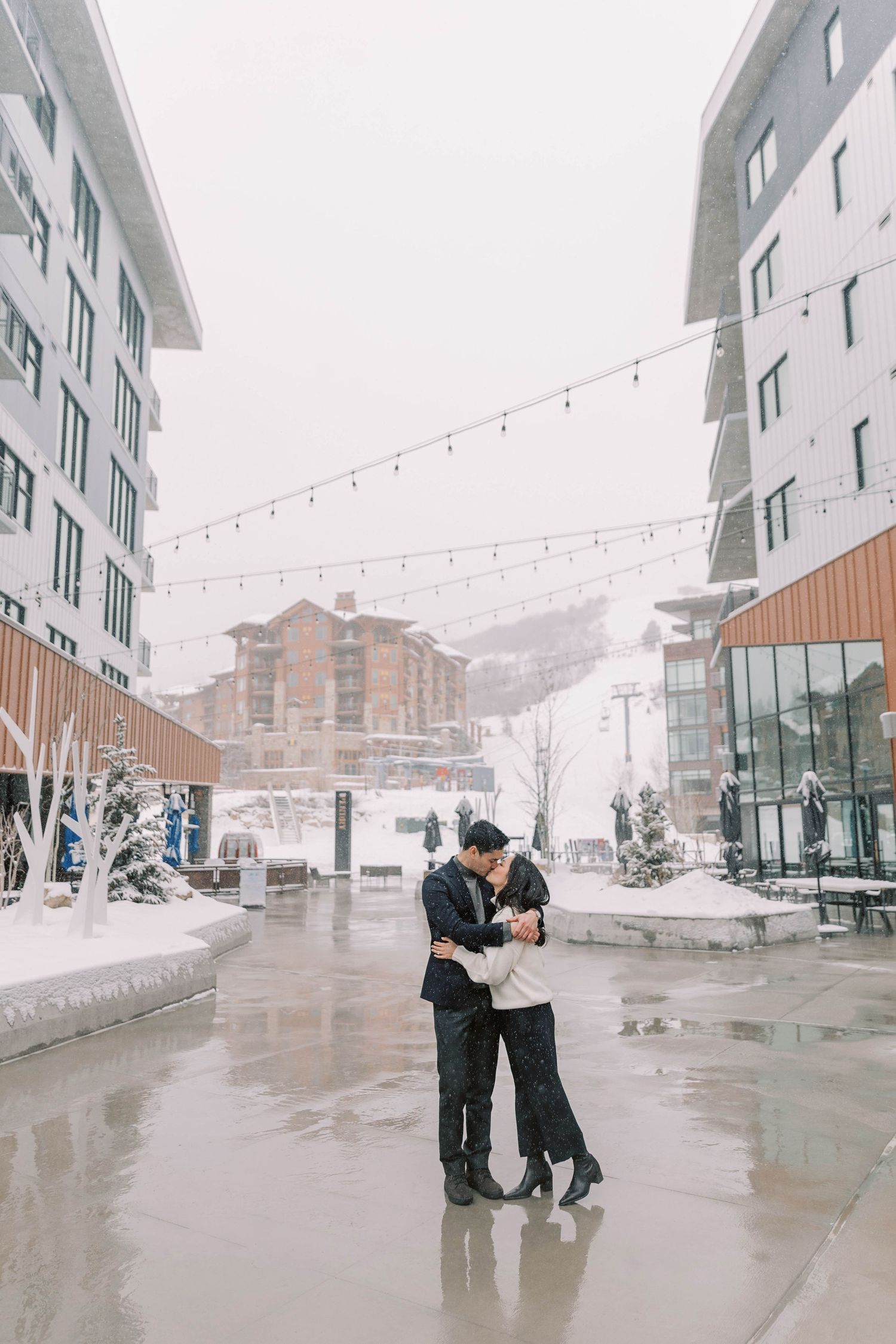 Winter engagement photo with string lights and snowy mountain backdrop at the pendry park city.