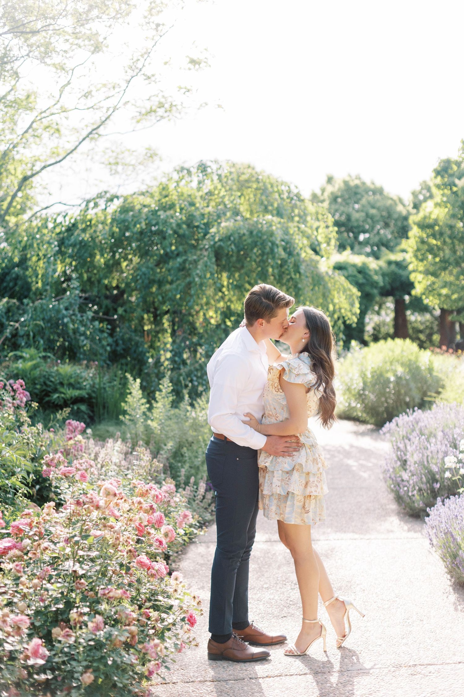 A romantic embrace on a sunlit garden path surrounded by summer blooms.