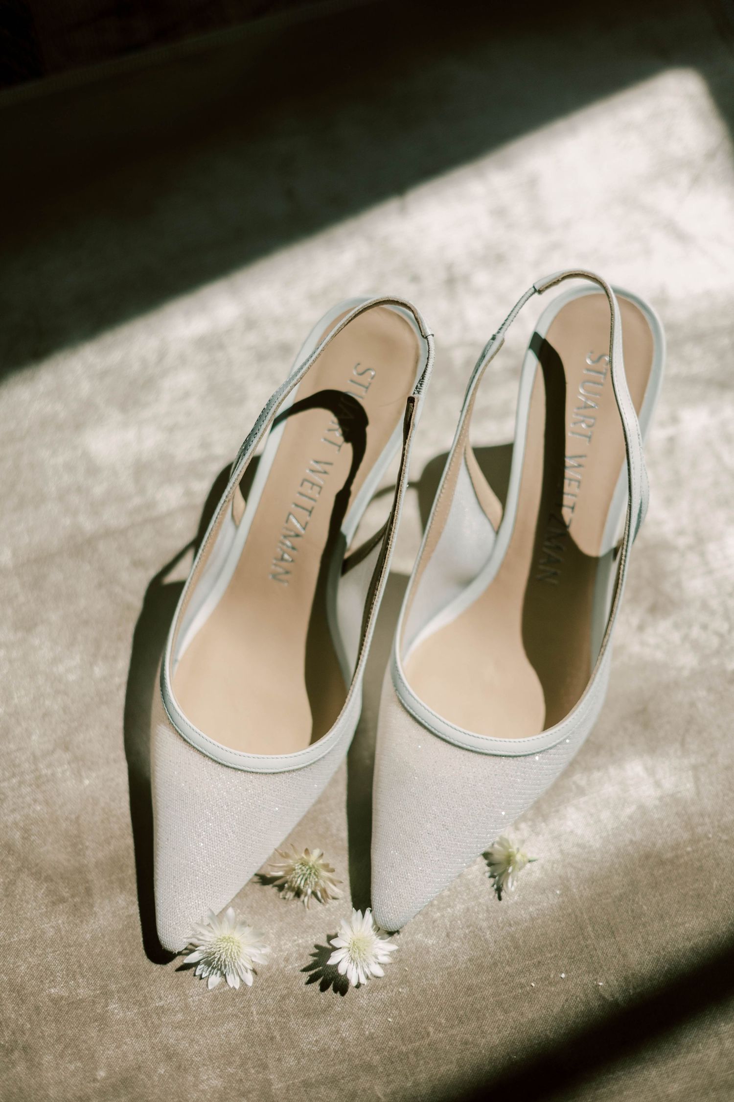 Elegant white bridal shoes with small daisy flowers on a textured surface.