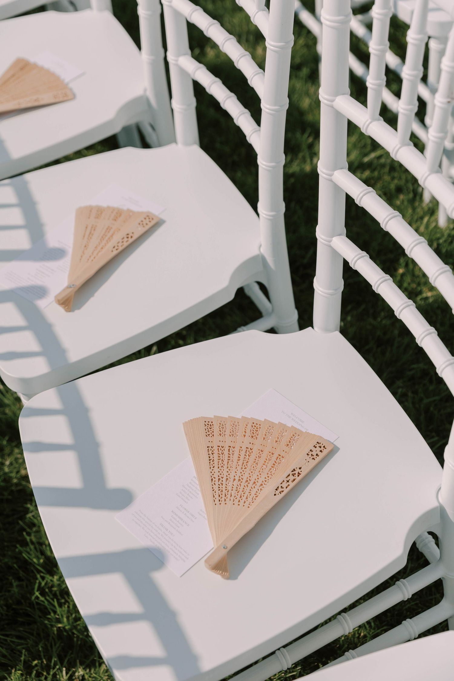 Decorative paper fans placed on white ceremony chairs.
