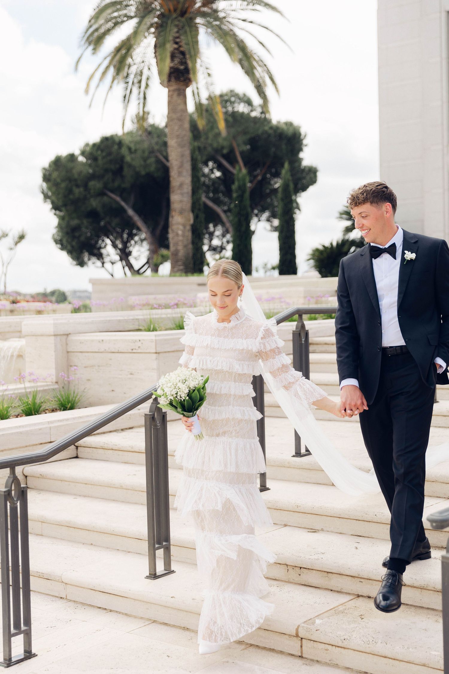 wedding Couple descending white stone steps of temple holding hands in formal attire at rome italy lds temple.