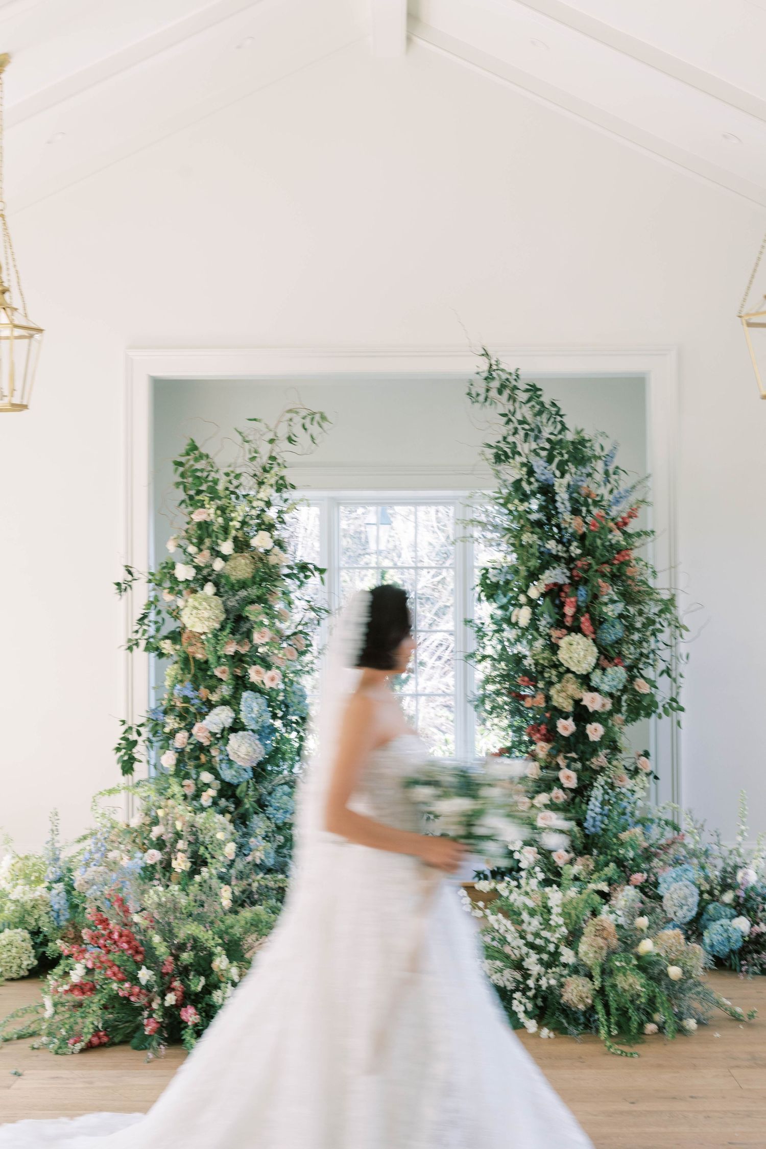 A flowing white wedding dress captured in motion between floral archways.