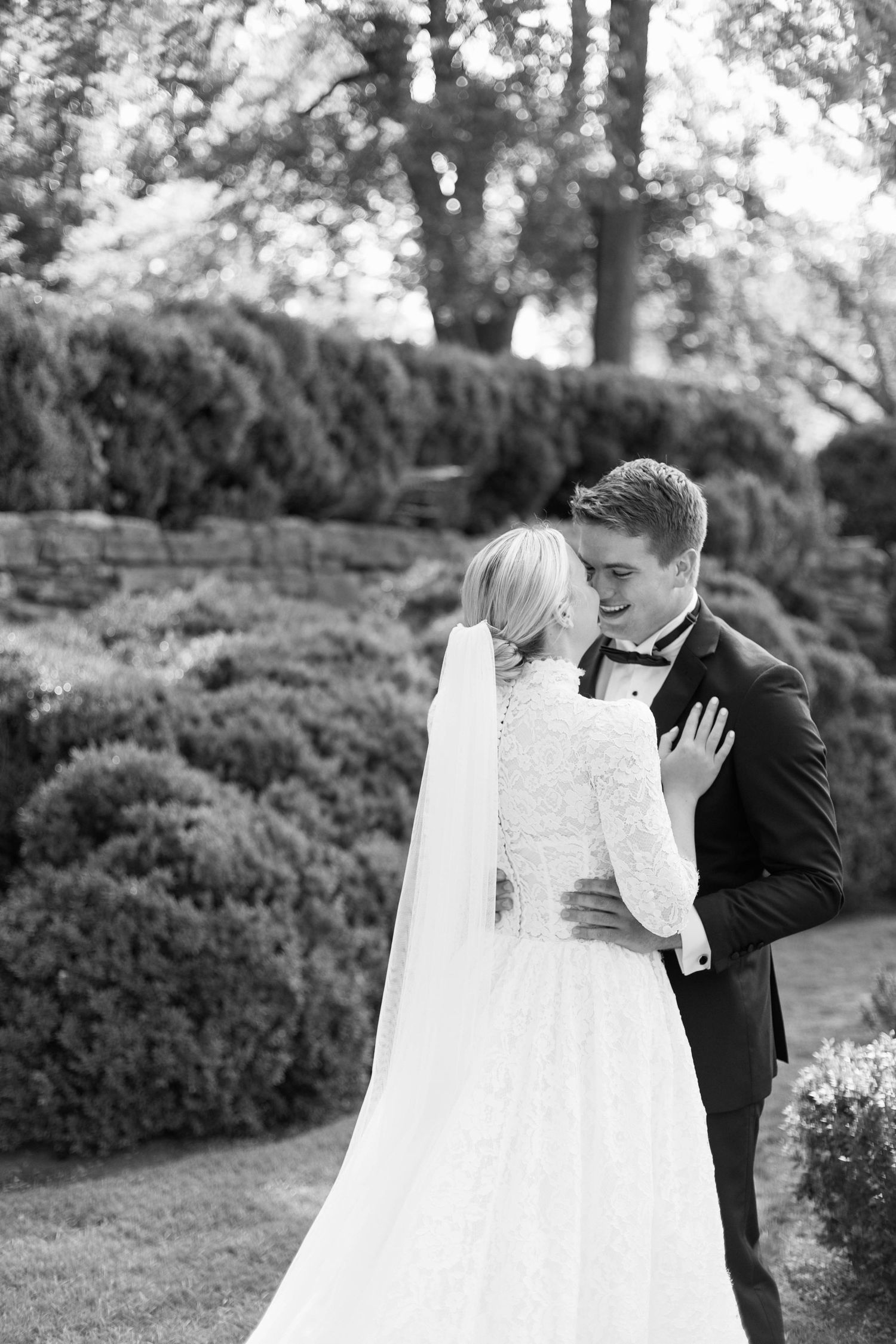 A romantic black and white wedding portrait with bride in lace dress and groom in tuxedo among garden hedges at Cheekwood Estate.