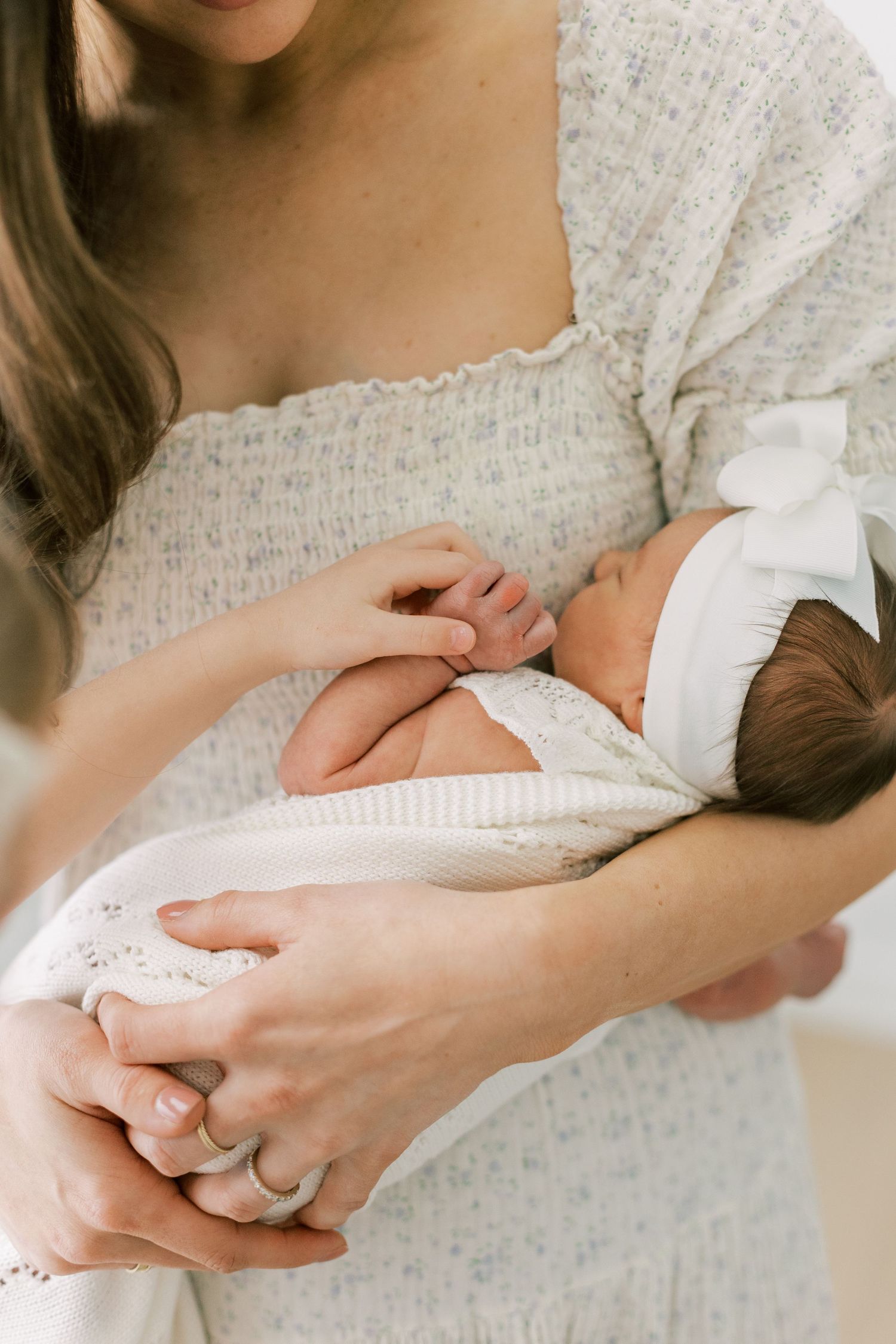 Tender moment of mother cradling newborn baby in textured white dress.