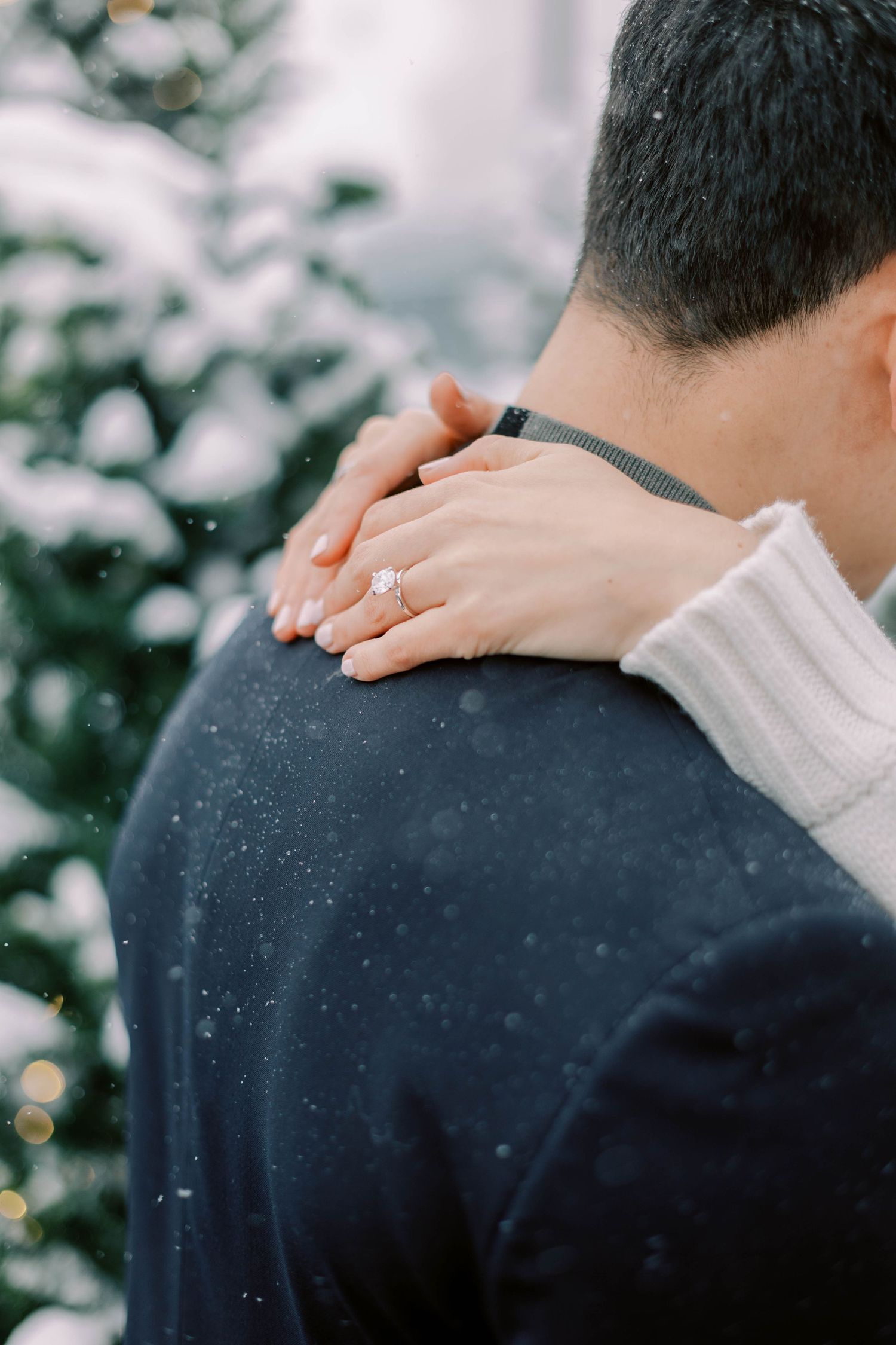 Hand wearing engagement ring rests on shoulder during snowy proposal photos at the pendry park city.