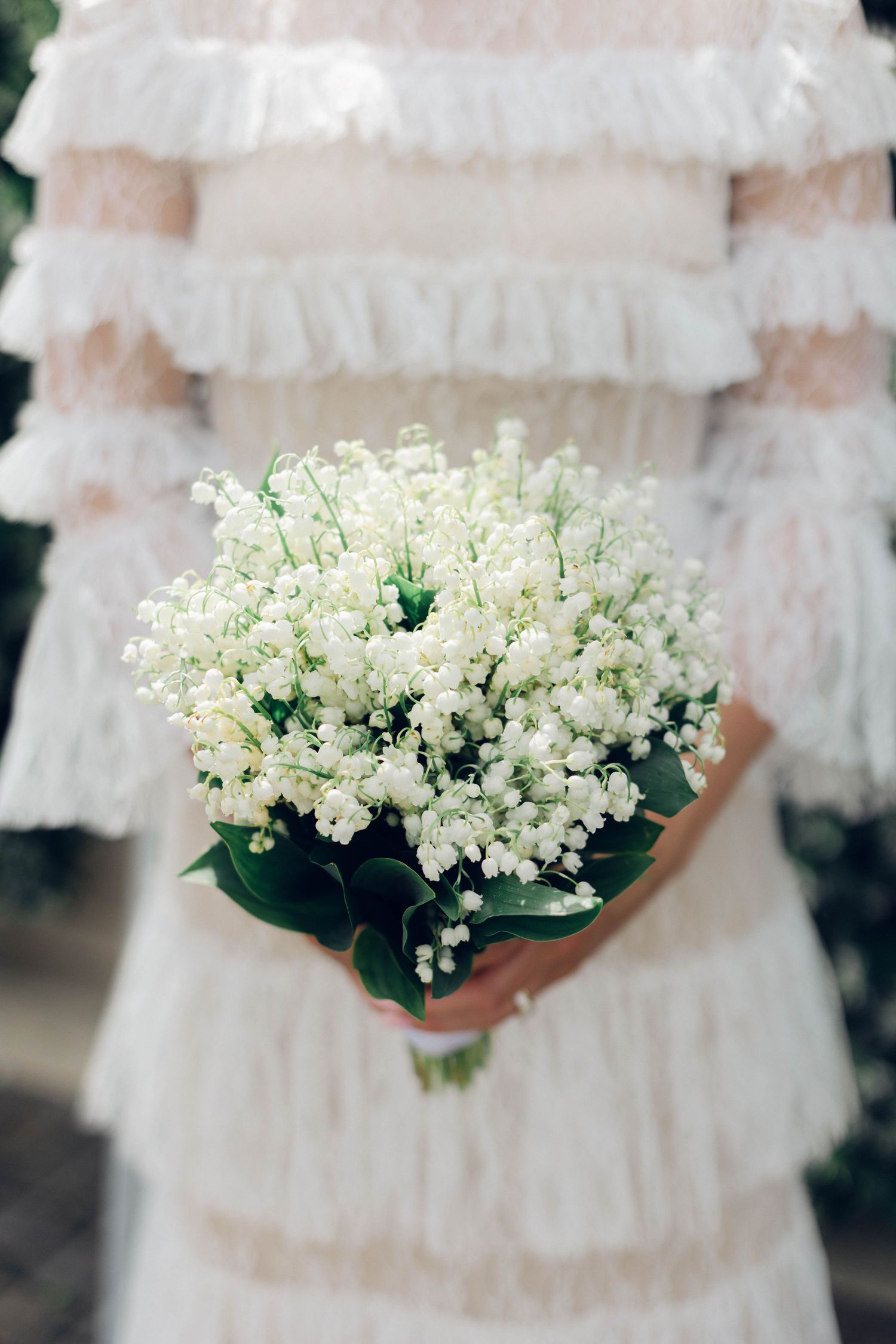A delicate white lily of the valley bridal bouquet against a ruffled wedding dress.