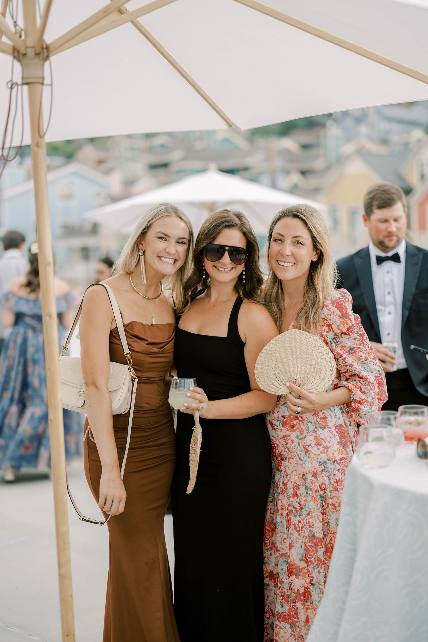 Guests in formal attire posing under a white canopy at an outdoor celebration.