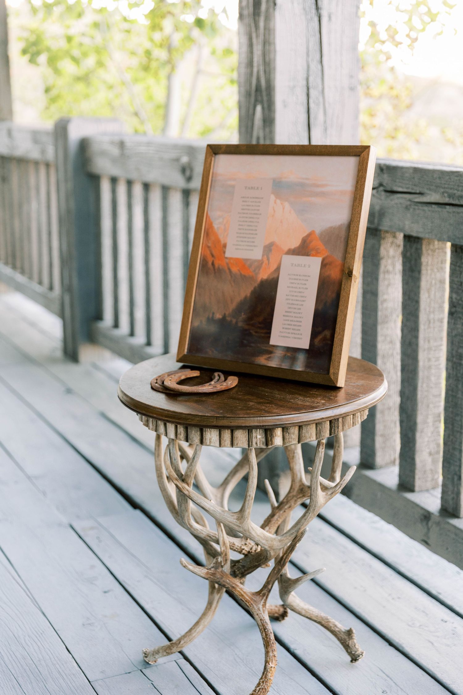 Framed seating chart on an antique metal side table with ornate details sits on a wooden deck.