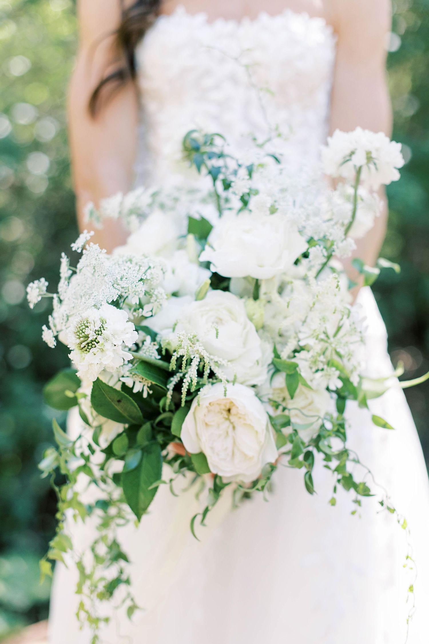 Close-up of romantic white and green wedding bouquet with trailing greenery.