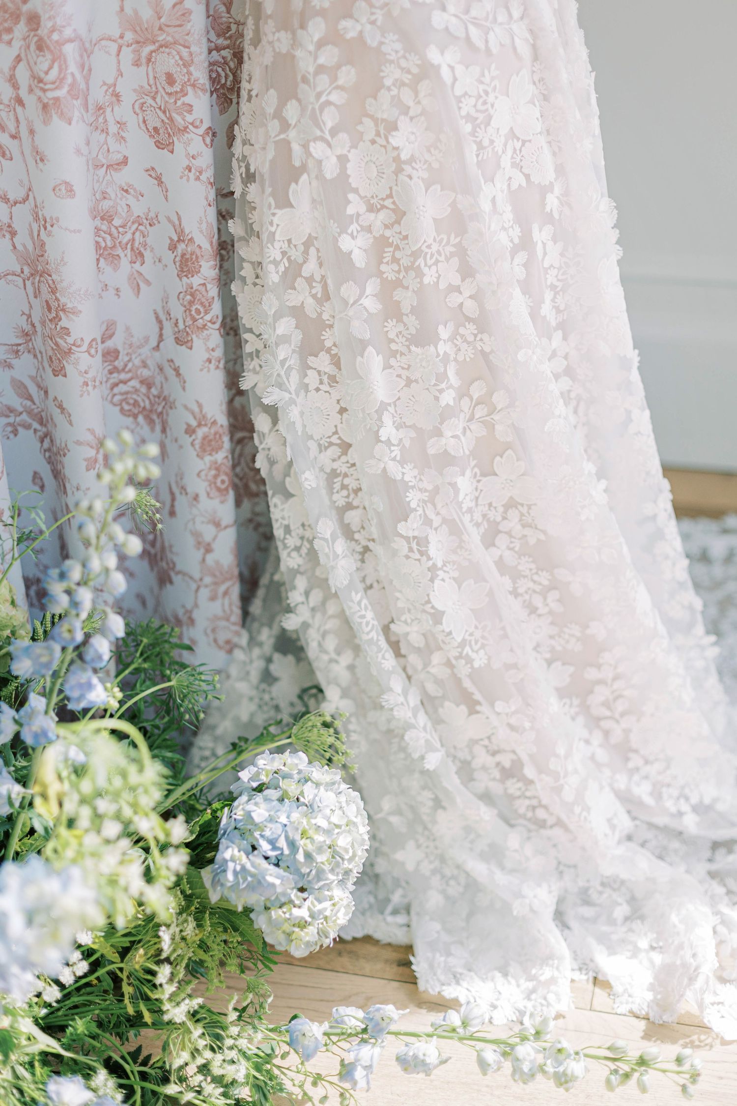 Delicate white lace fabric drapes beside blue hydrangeas and floral arrangements.