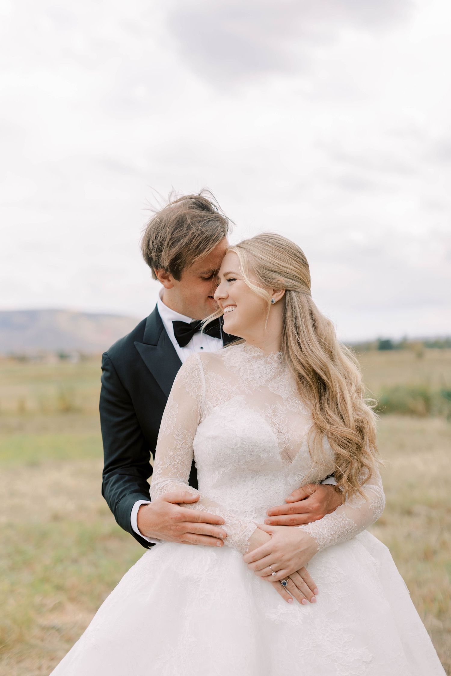 A tender moment between newlyweds in a scenic mountain field.