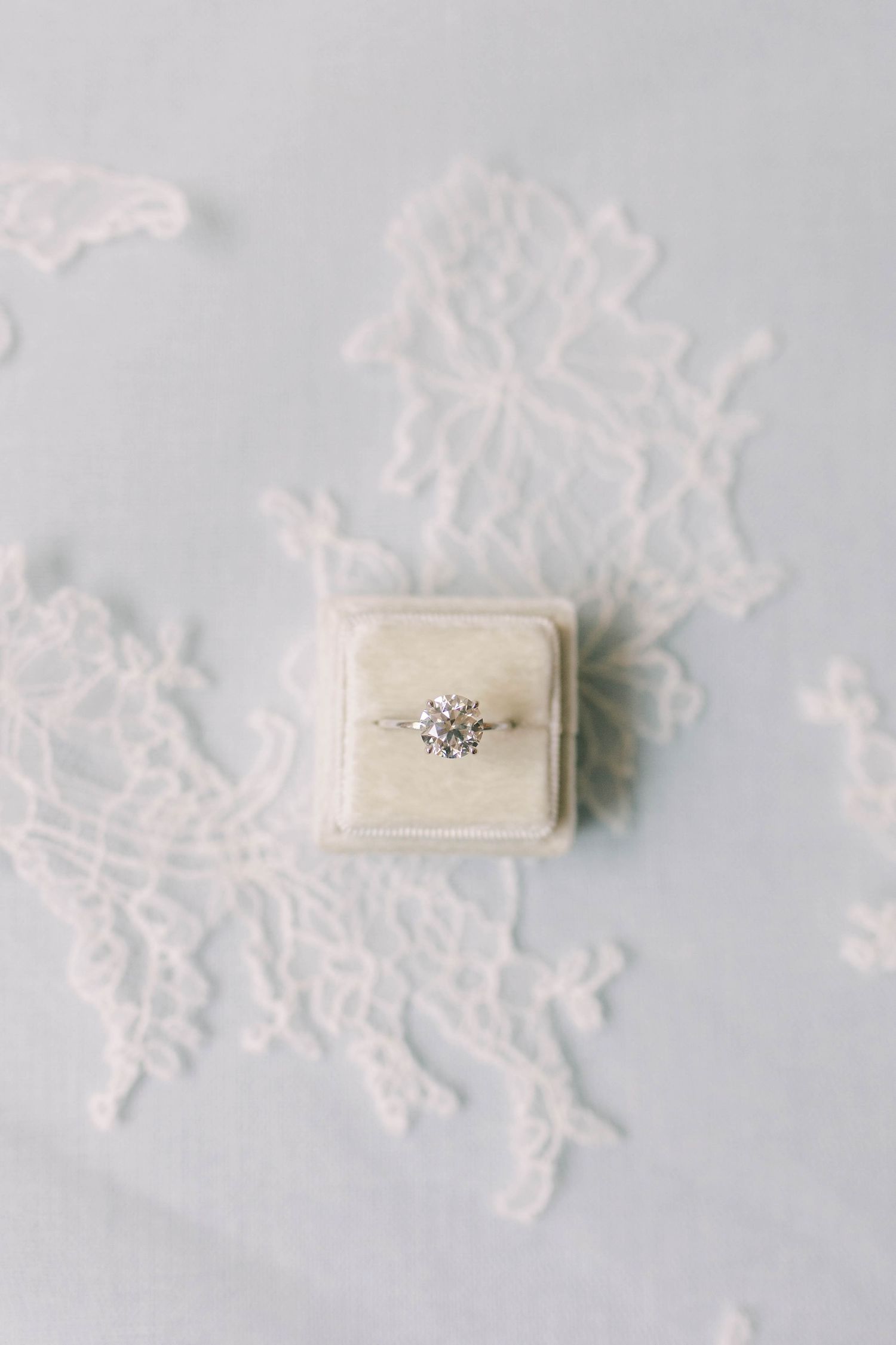 A sparkling diamond engagement ring in a velvet box on delicate white lace.