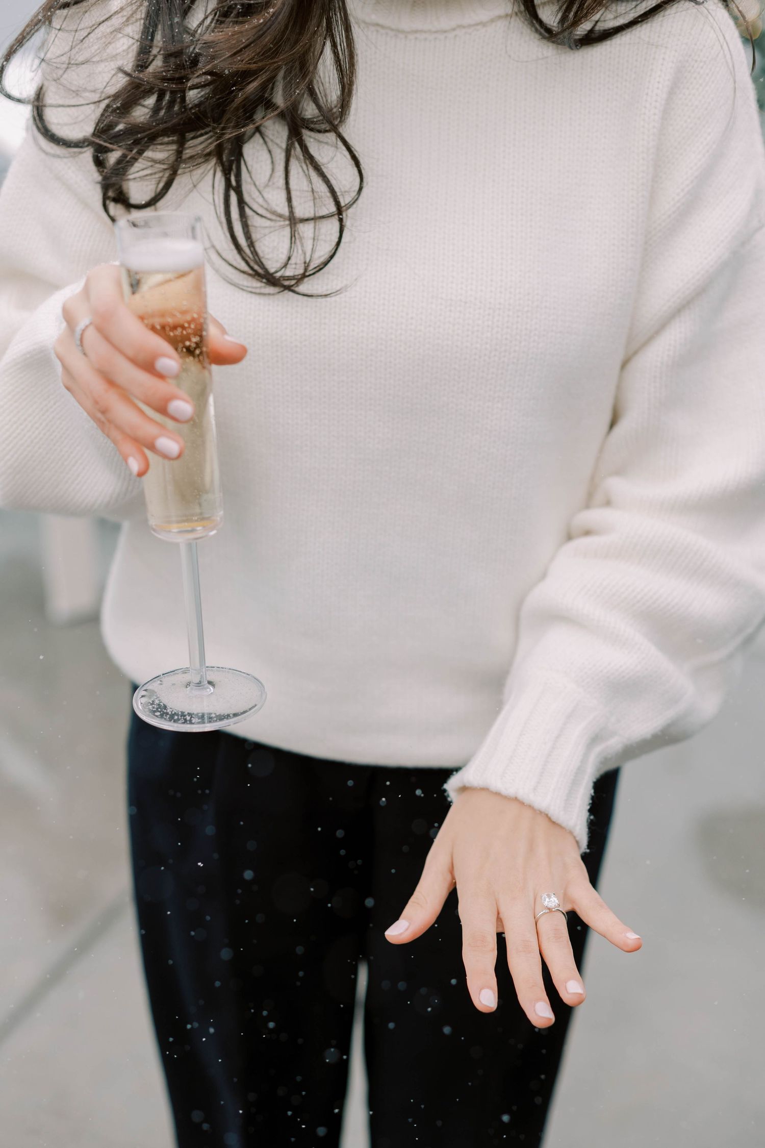 Person in white sweater holding champagne glass wearing sparkly black pants.