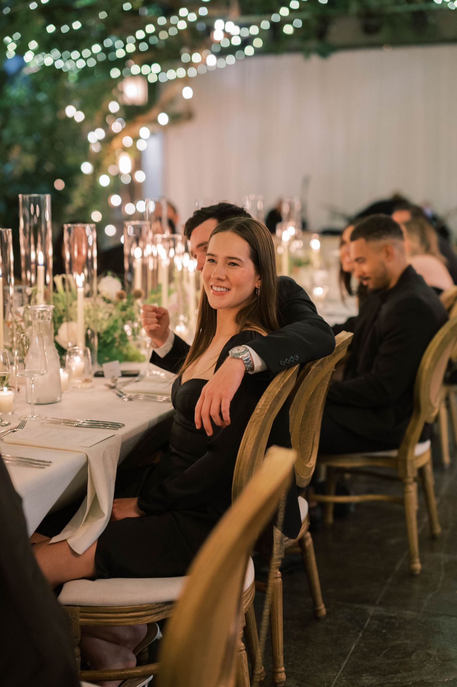 Wedding reception guests enjoying dinner under twinkling lights in an elegant outdoor setting.