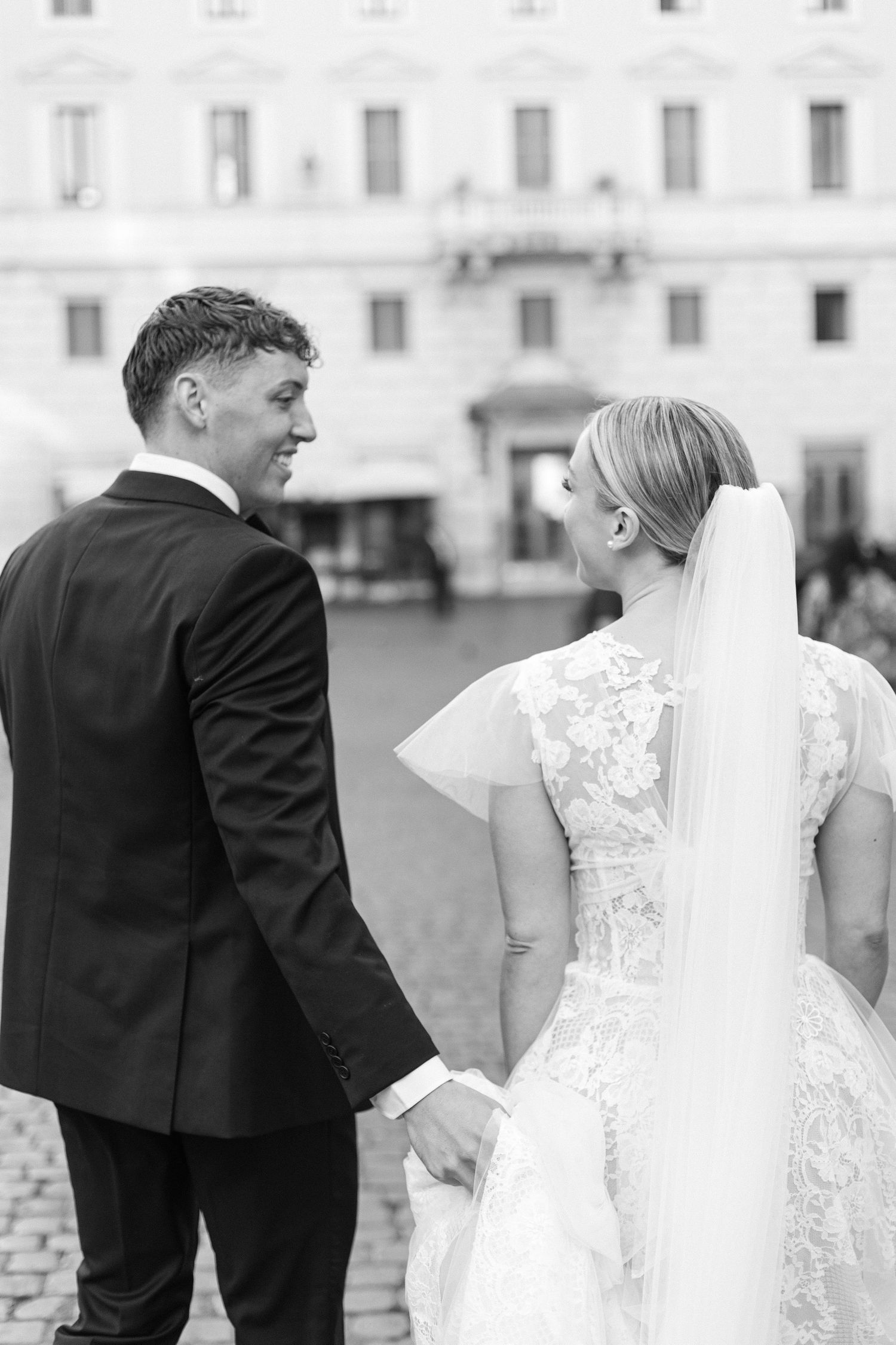 Wedding couple shares an intimate moment against a white building facade.
