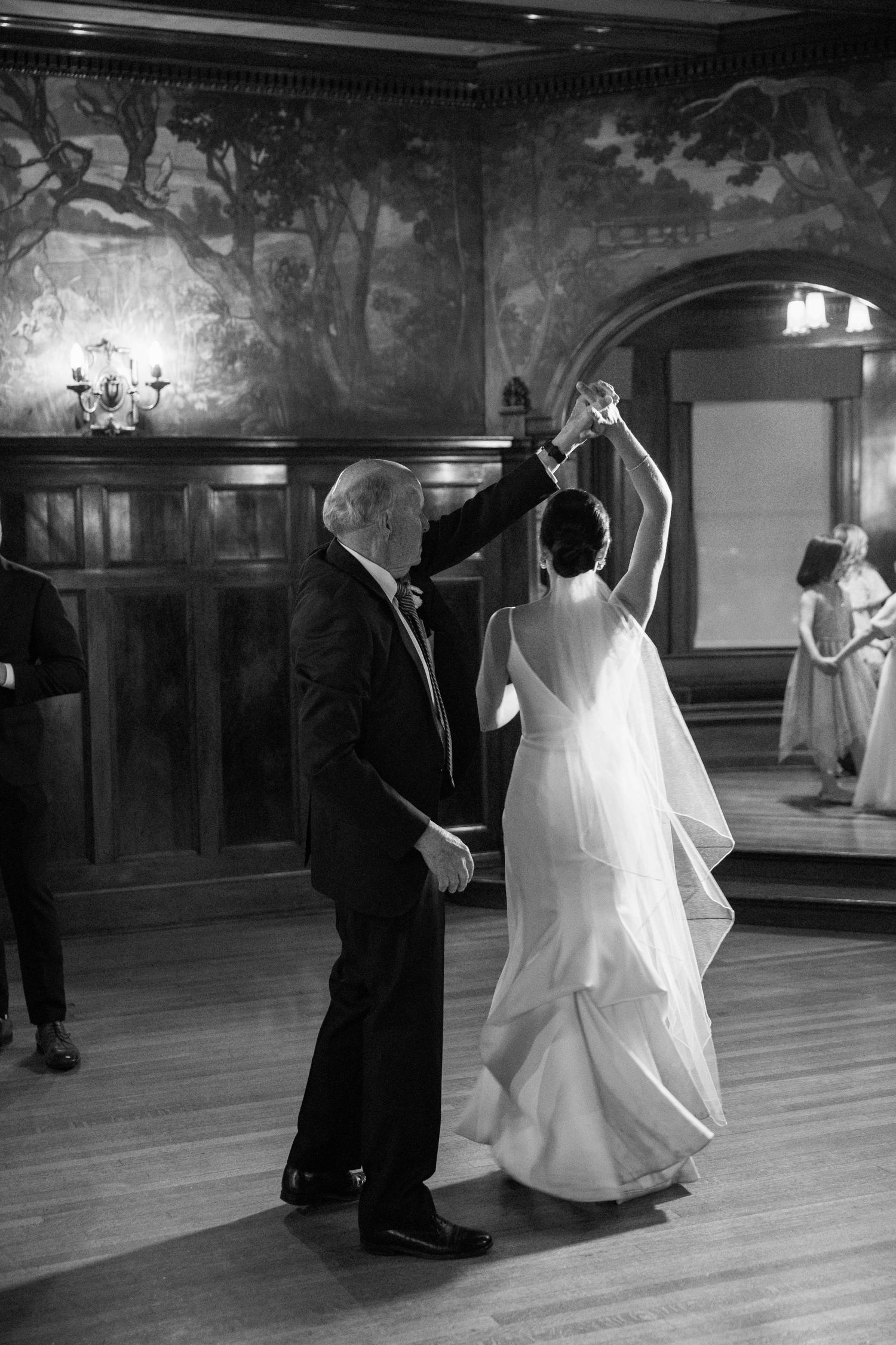 A joyful dance moment captured in black and white with elegant wall murals in the background.