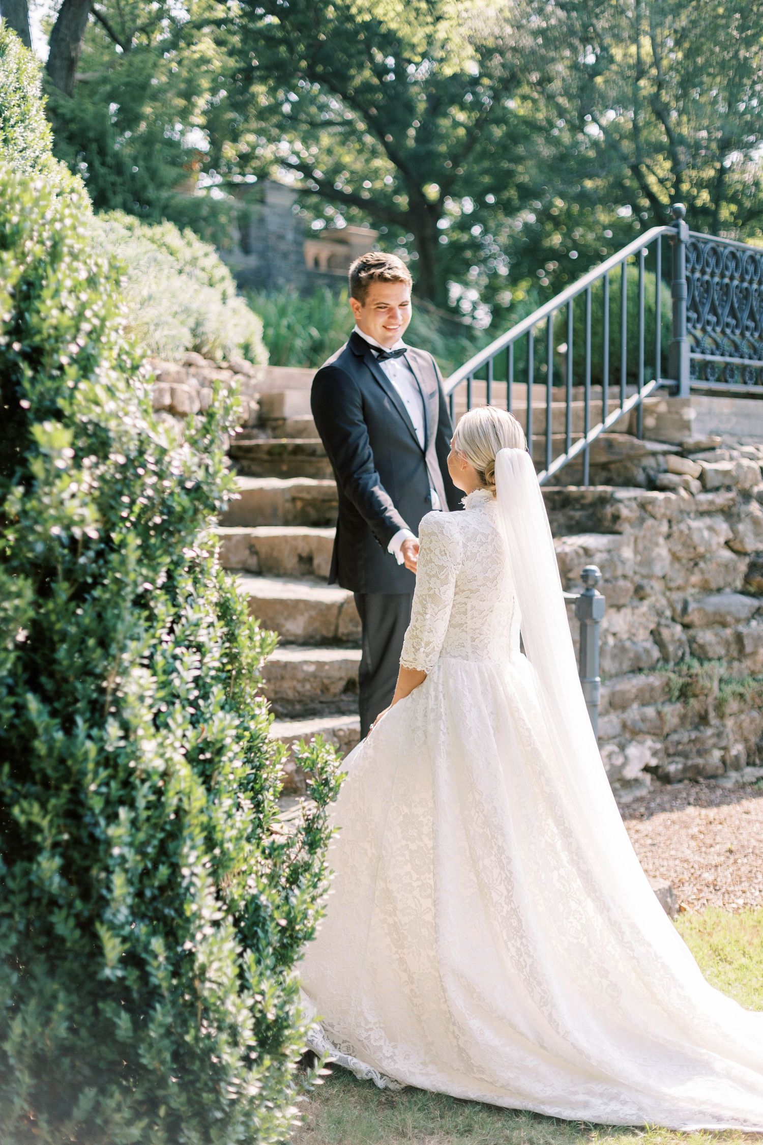 Wedding couple poses on stone garden steps surrounded by lush greenery and ornate railings of Cheekwood Estate.