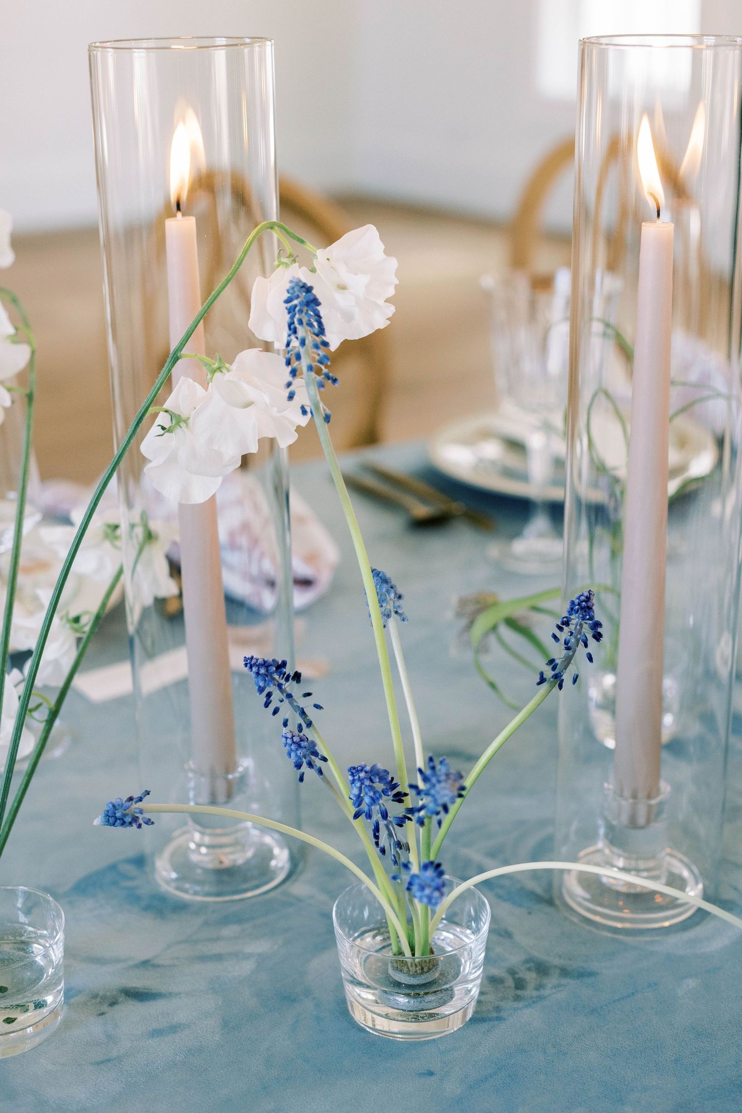 Close-up of wedding table centerpiece with glass candleholders and delicate blue and white flowers.
