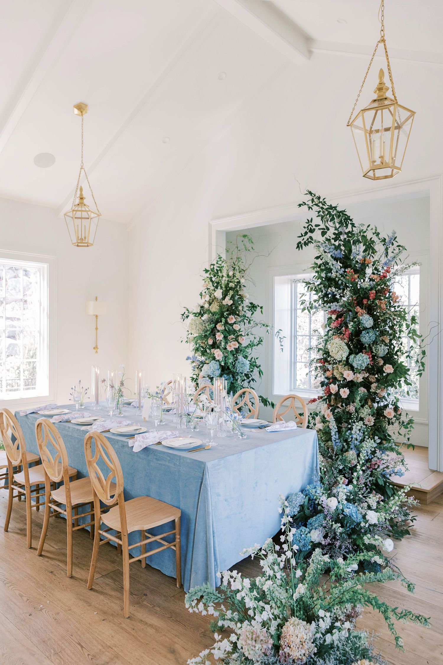 Elegant wedding table setting with blue linens, gold chairs, and dramatic floral arrangements.
