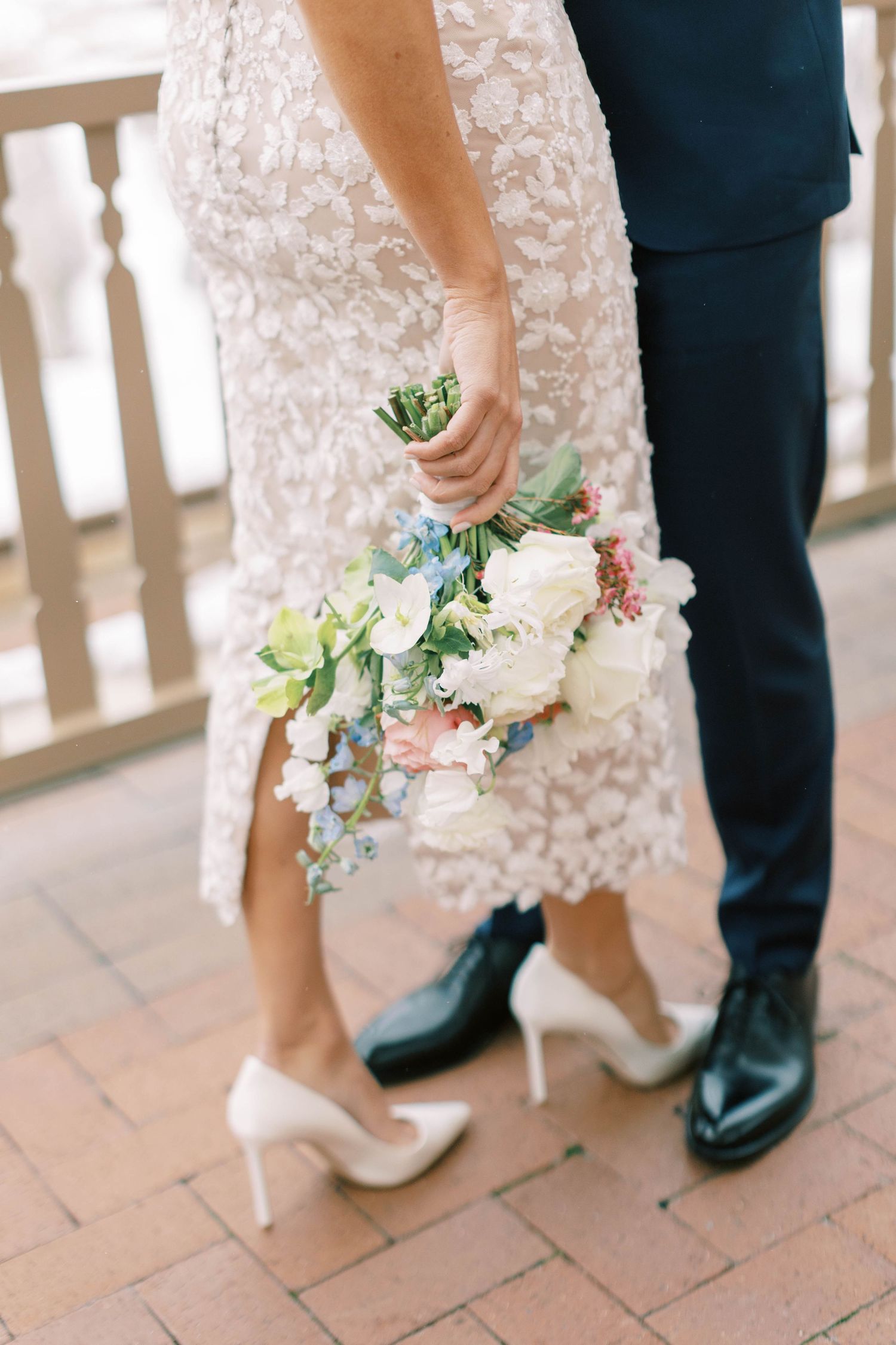 Close-up of wedding couple's feet and pastel bouquet on brick terrace.