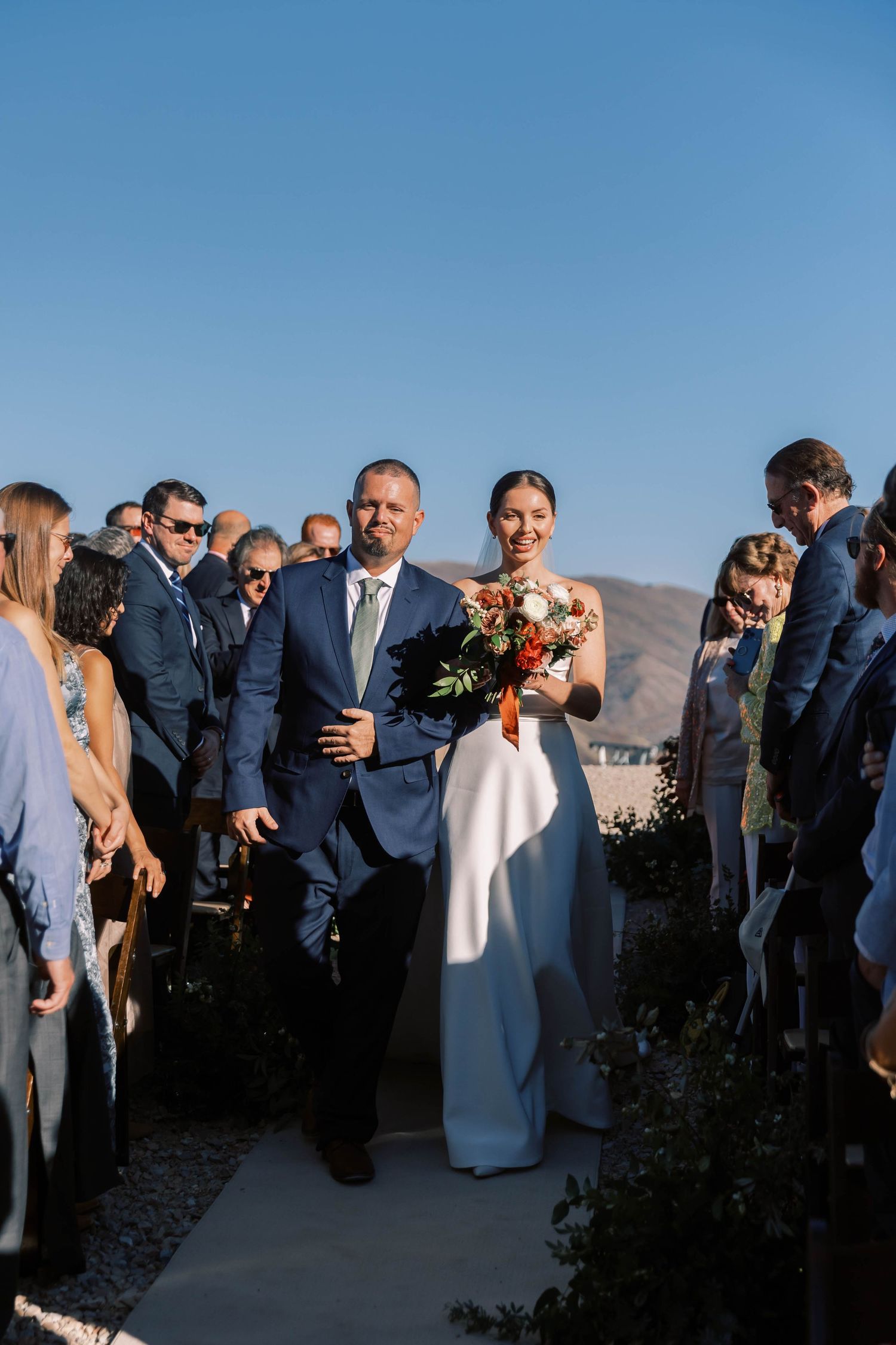 Wedding processional on mountain overlook with guests lining scenic pathway.