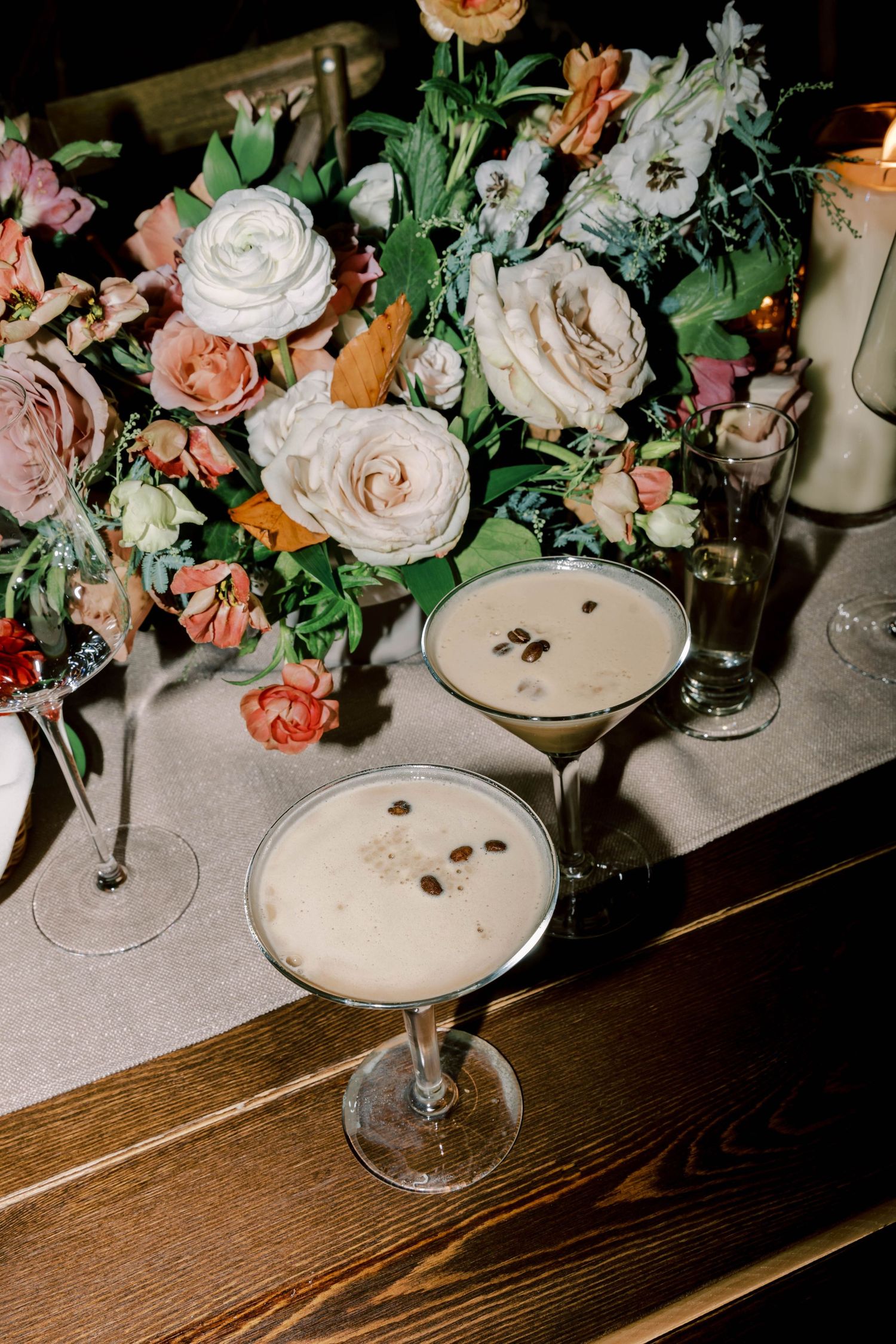 Elegant cocktails with foam garnish next to a floral centerpiece with pink and coral roses.