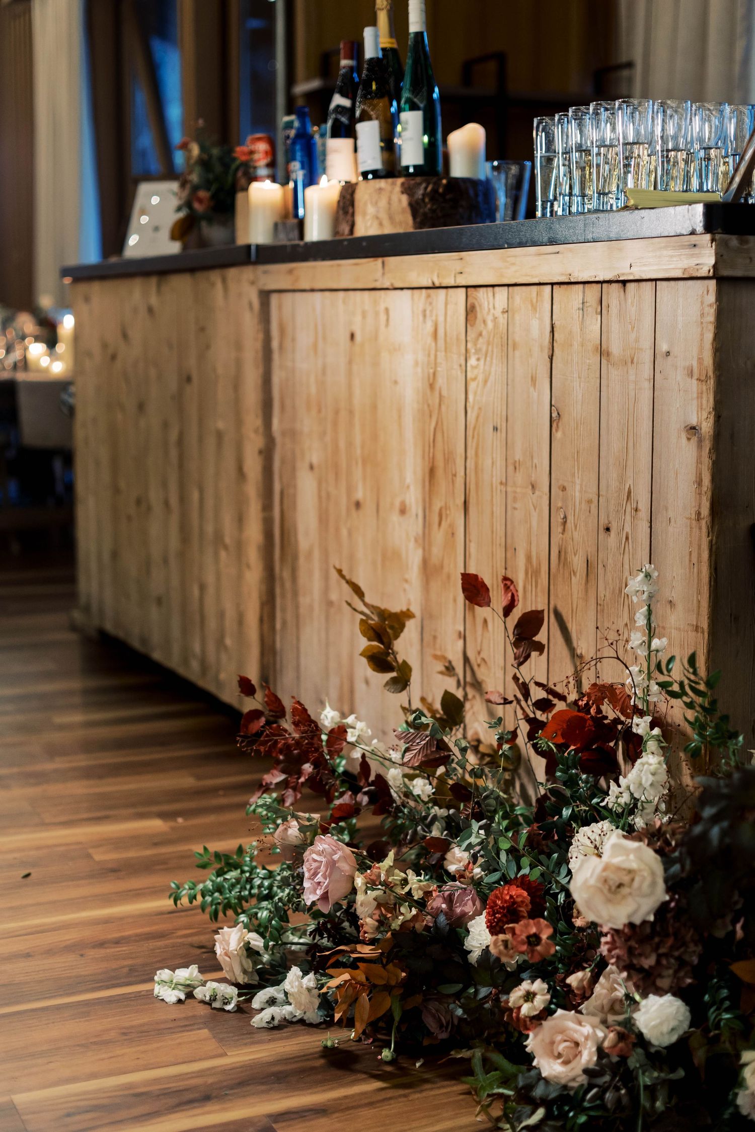 Rustic wooden bar decorated with romantic floral arrangements of roses and autumn foliage.