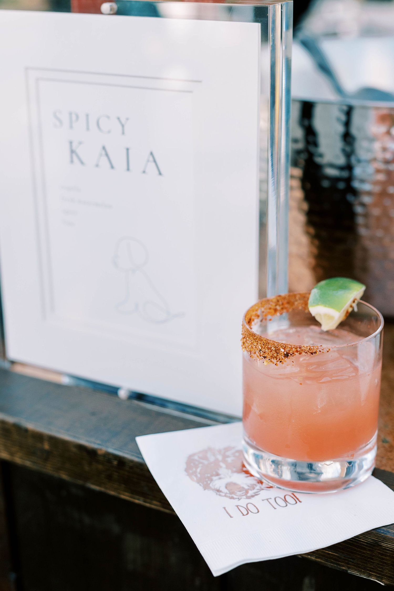 Pink spicy cocktail with salted rim next to Spicy Kala menu card.