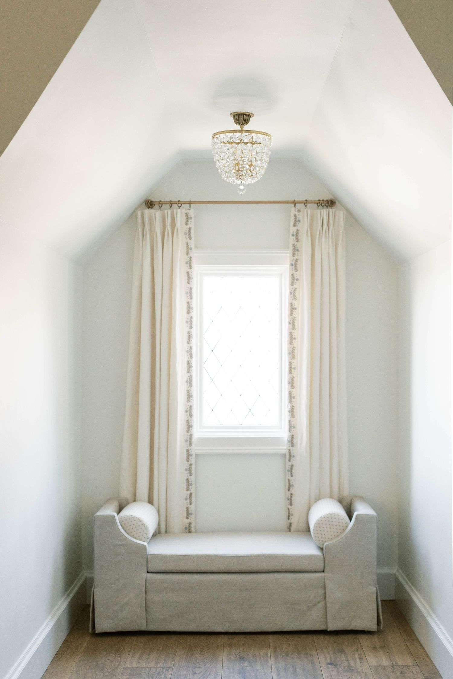 Minimalist attic nook with crystal chandelier and white upholstered bench.
