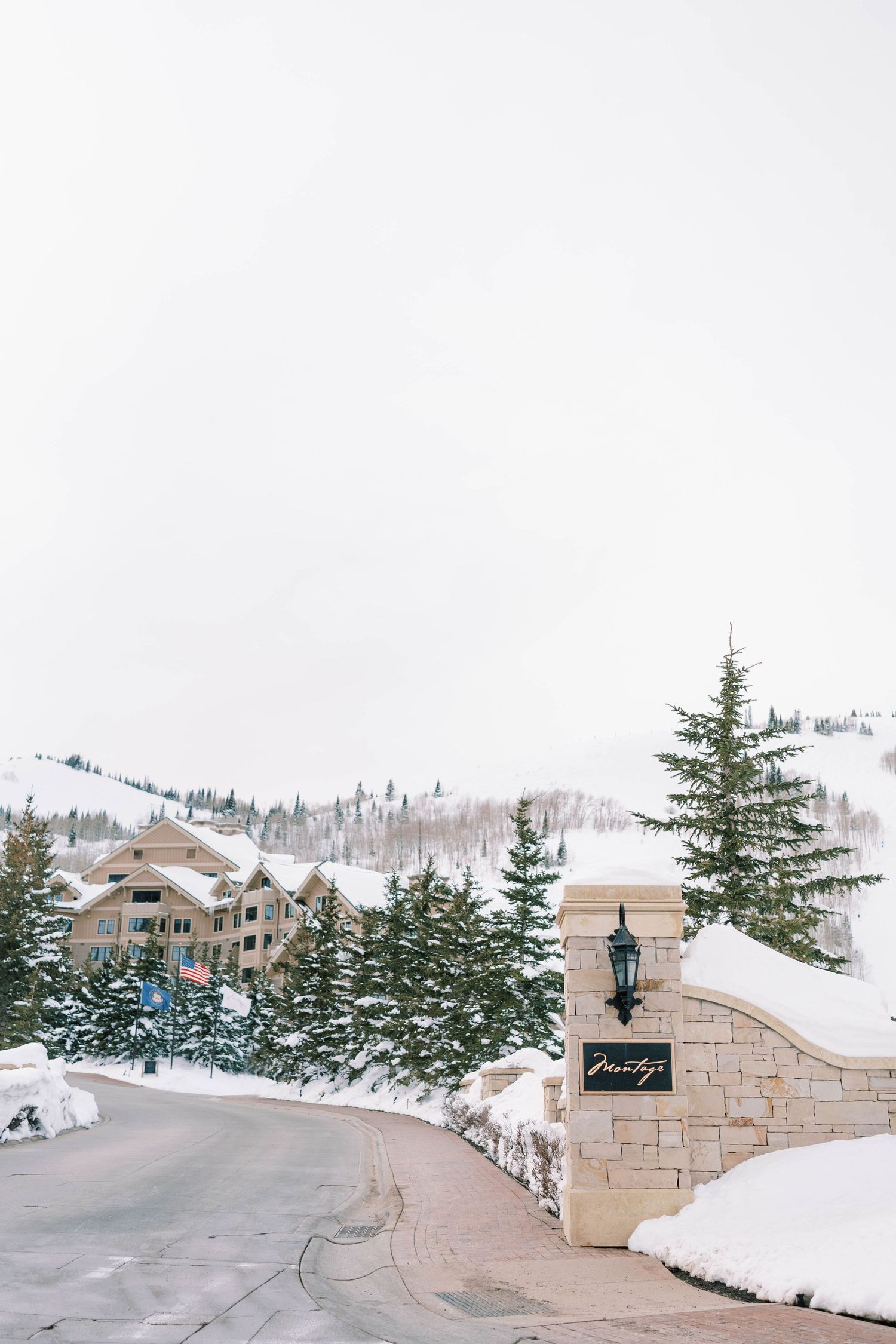 Snowy mountain resort entrance with stone pillars and evergreen trees lining a curved road at the montage deer valley.