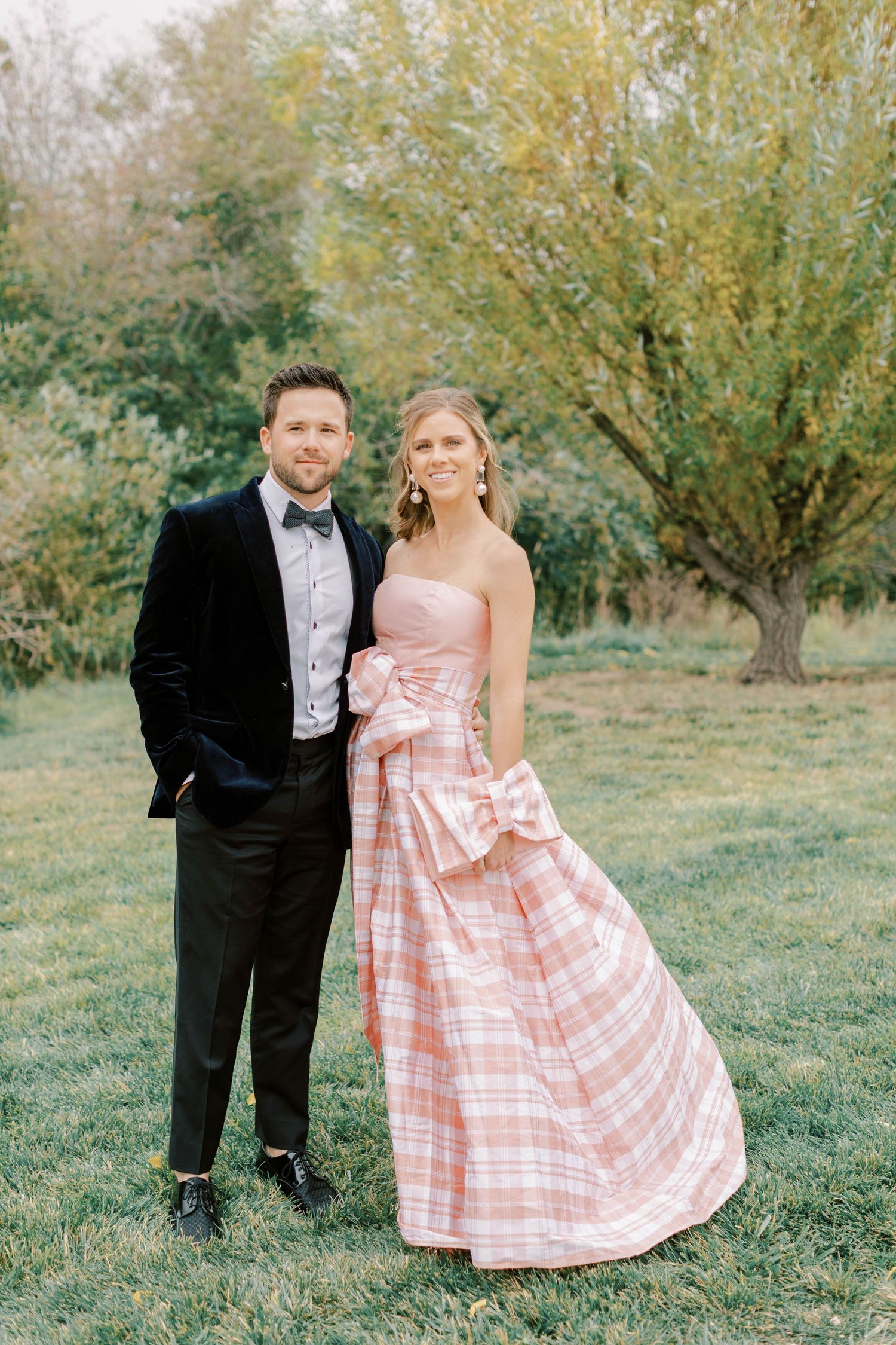 Couple in formal attire poses outdoors, bride wearing pink plaid gown.