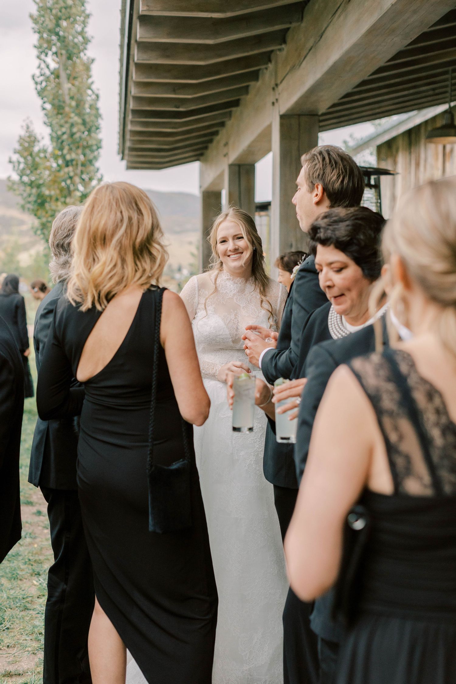 Wedding guests in black dresses socializing during outdoor reception.