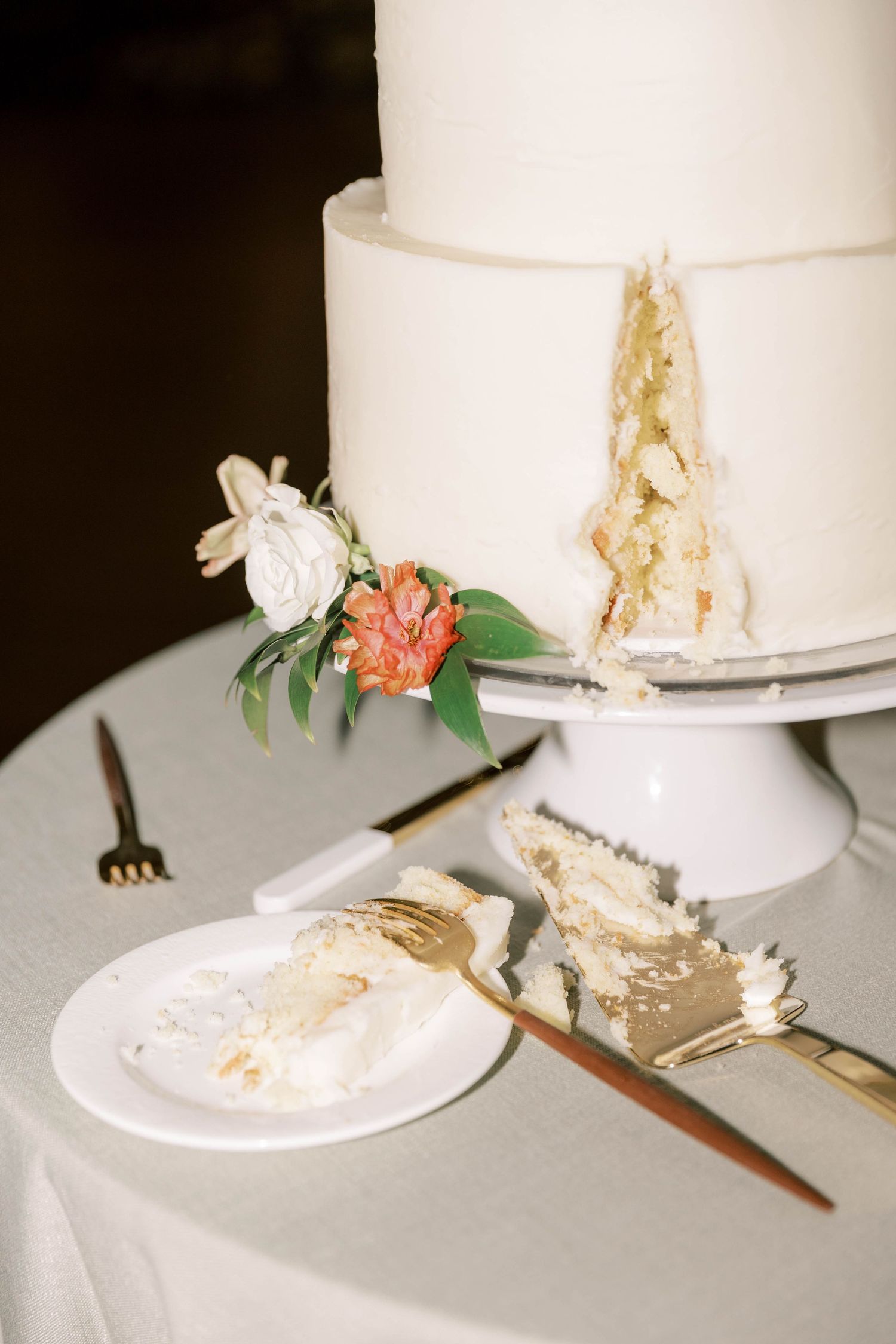 White wedding cake with delicate floral decorations and a slice being served on a plate.