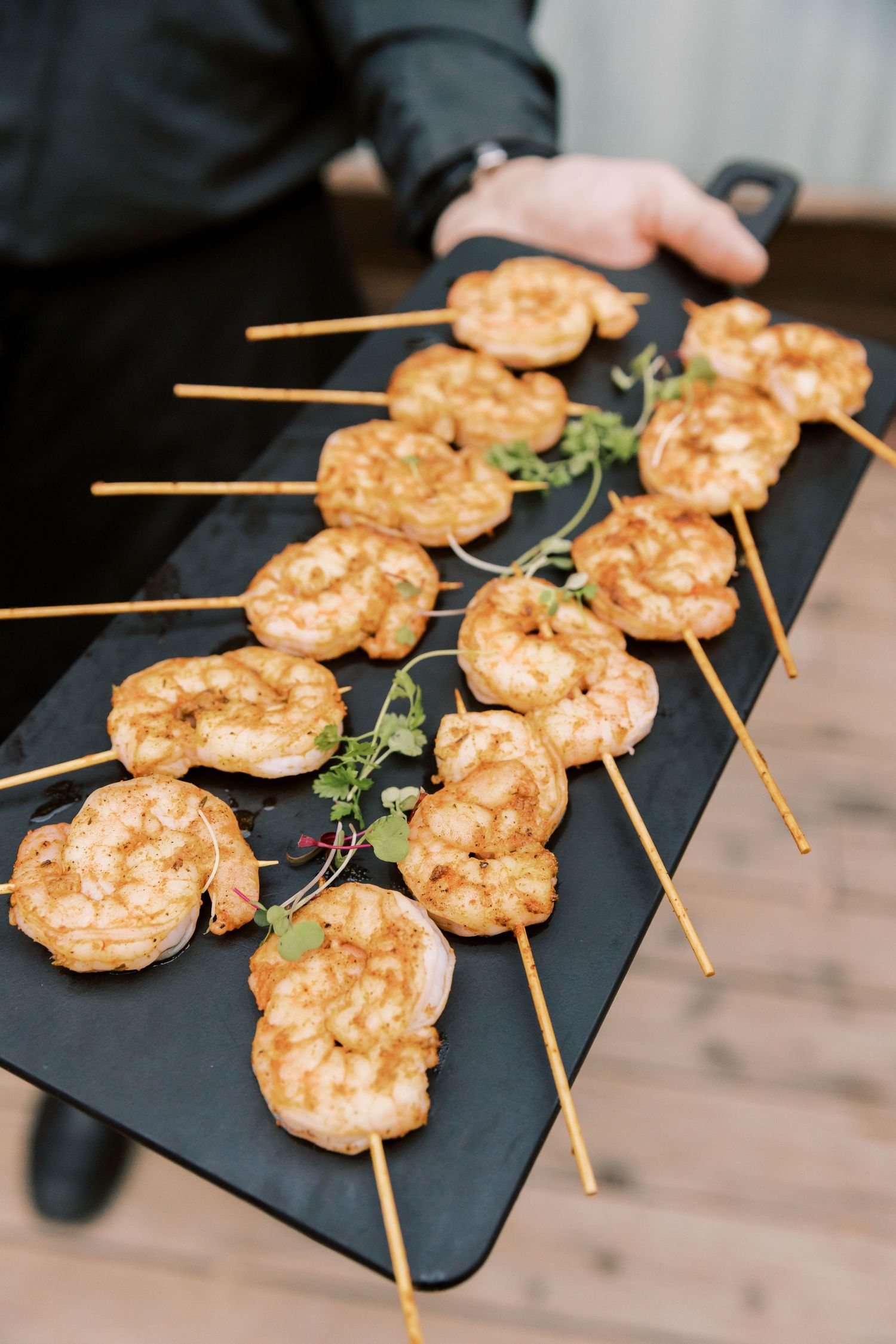 Grilled shrimp skewers garnished with fresh herbs displayed on a black serving platter.