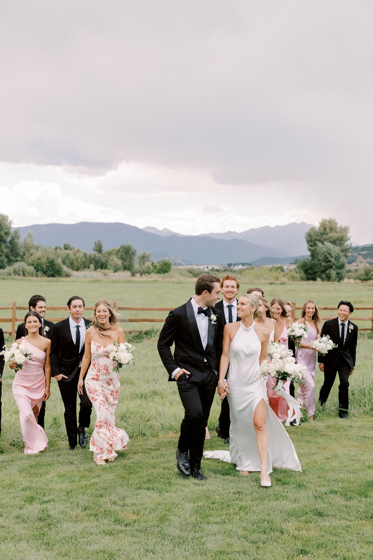 Wedding party walking together across a grassy field with mountain views in the background.