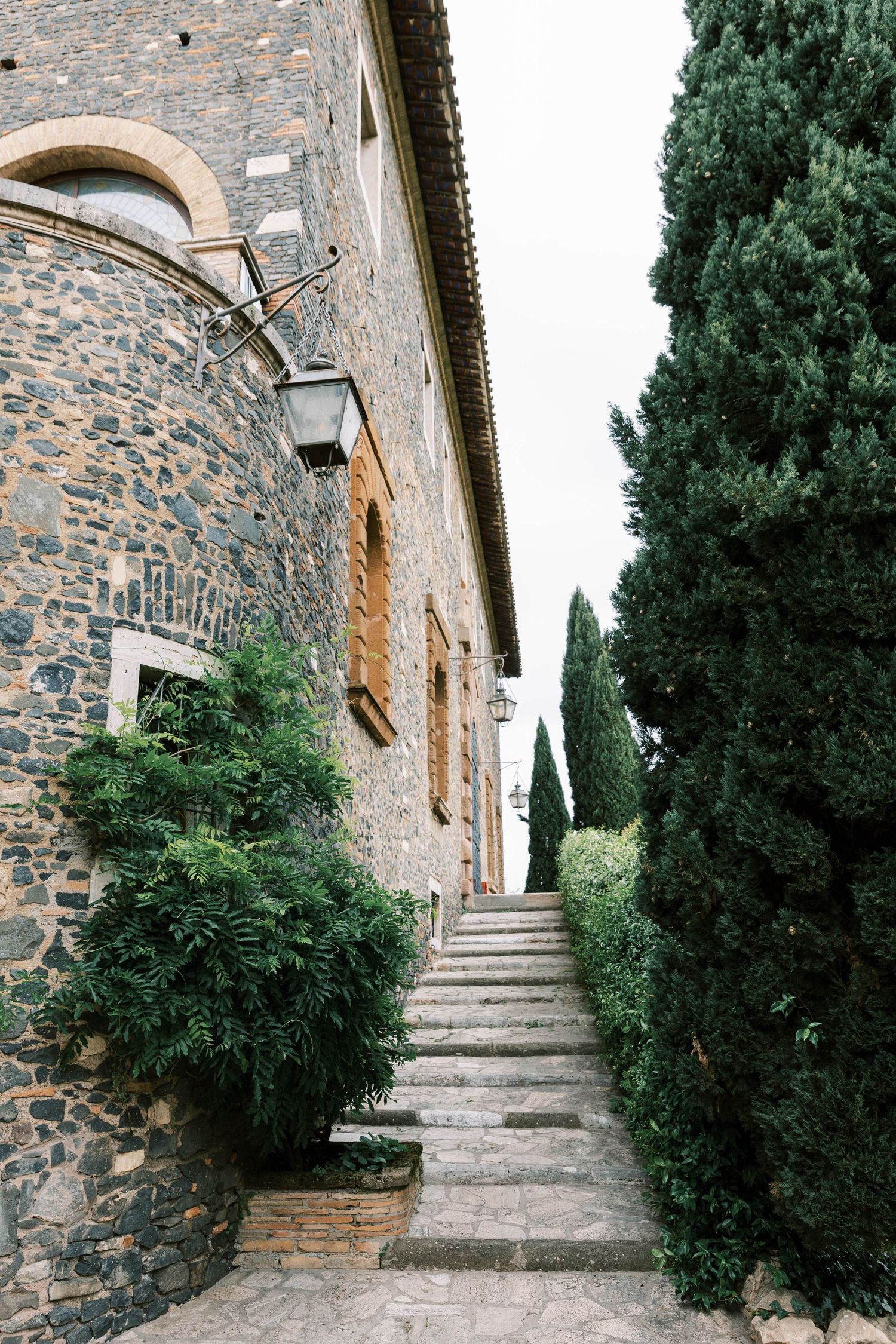 Stone steps lead up between cypress trees along a rustic Mediterranean building.