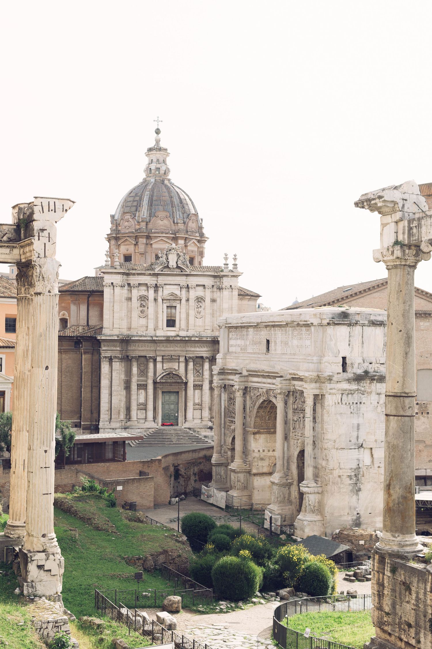 View of ancient Roman Forum with classical dome, columns and ruins against pale sky.
