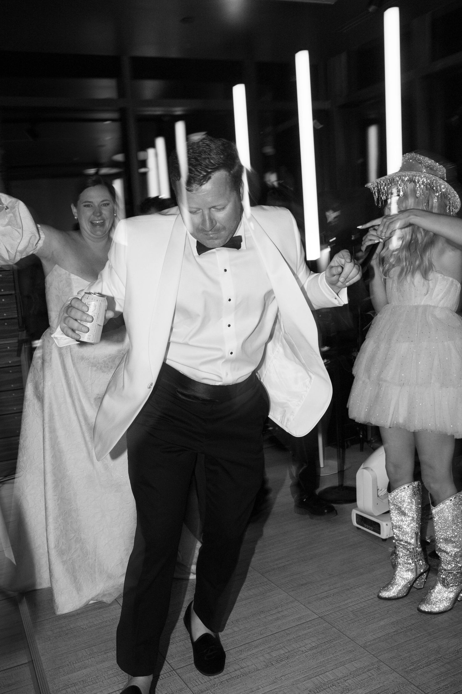Wedding guest dancing enthusiastically in white tuxedo at reception party.