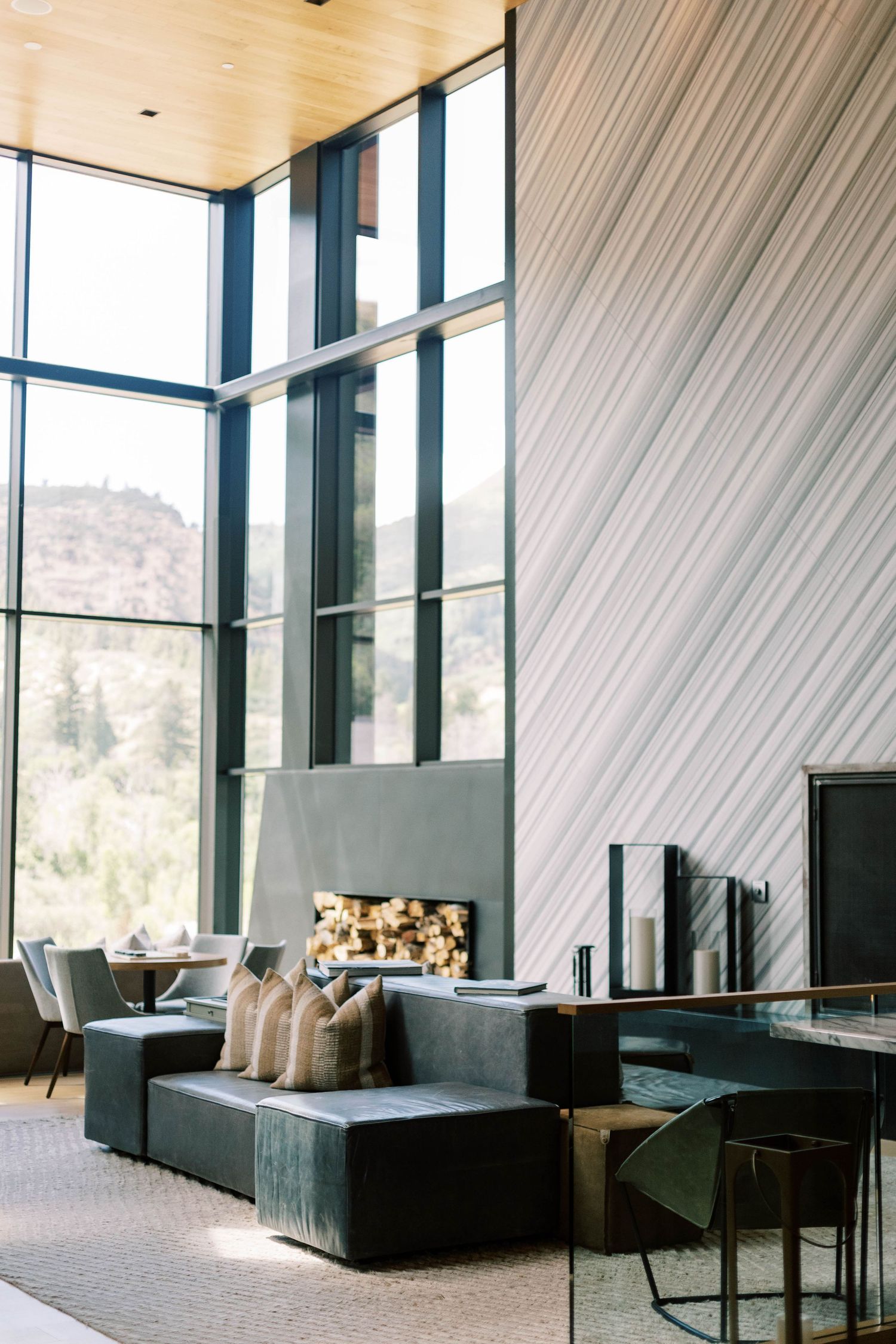 Modern lodge interior with floor-to-ceiling windows, firewood storage, and contemporary furnishings.