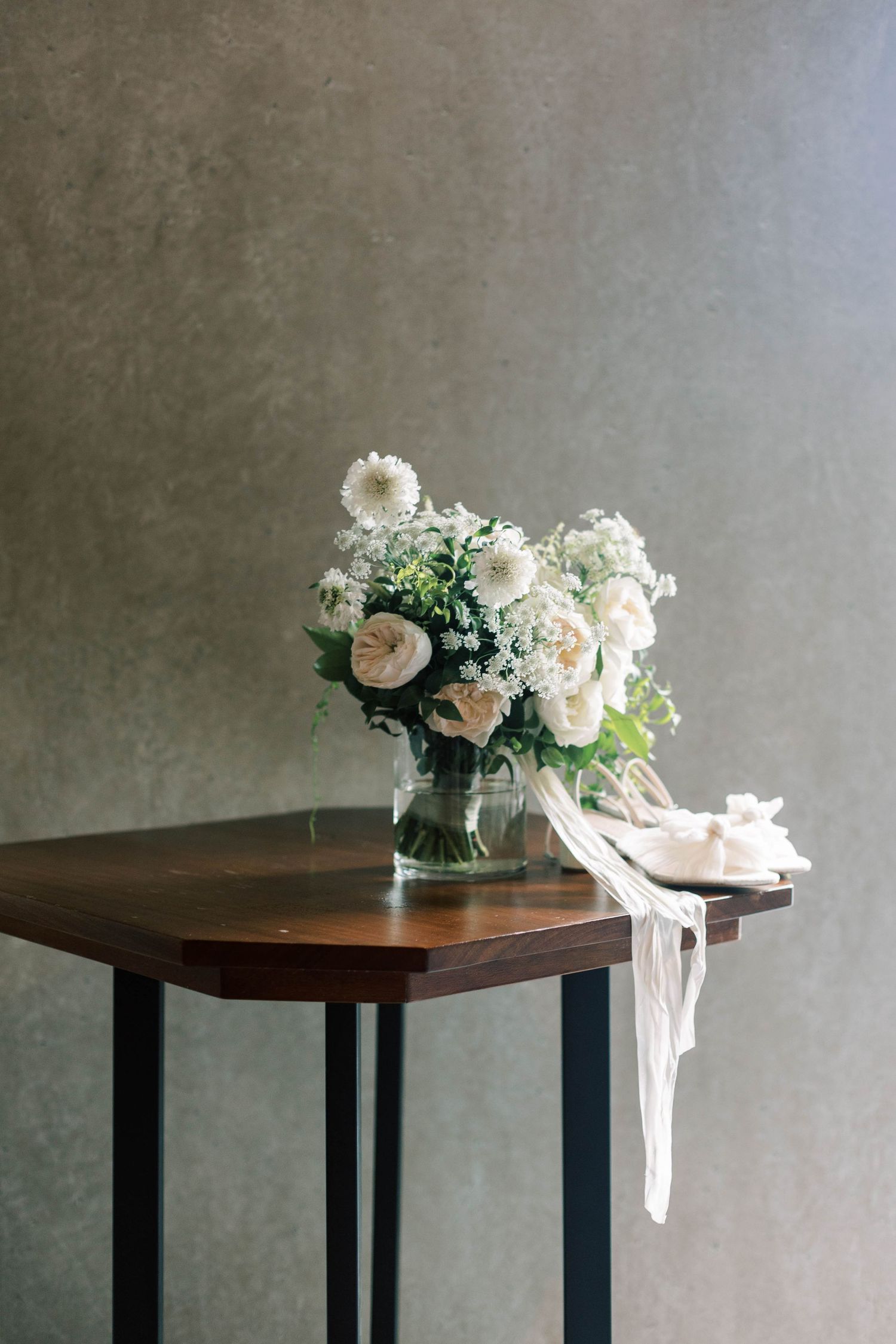 Elegant white floral arrangement in glass vase on wooden side table.