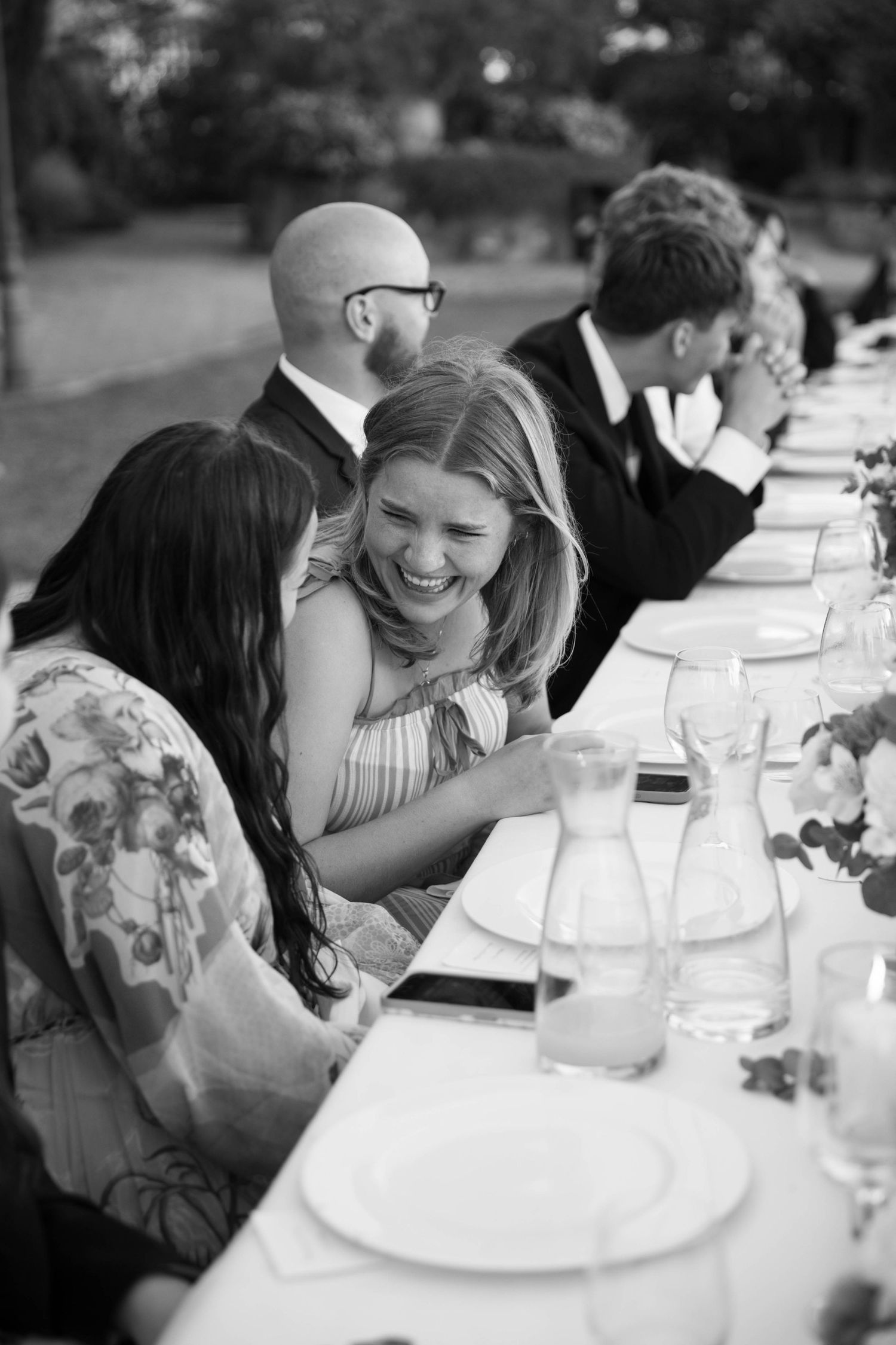 Candid black and white photo of guests enjoying conversation at an outdoor dining table.