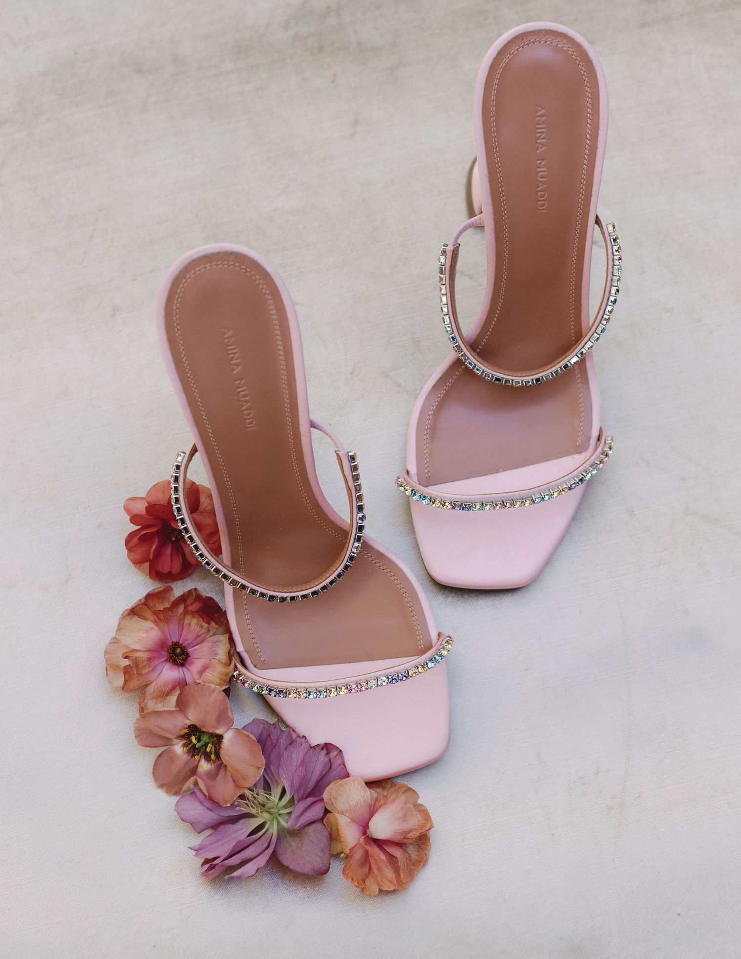 Pink sparkly heeled sandals with rhinestone straps displayed alongside colorful floral decorations.