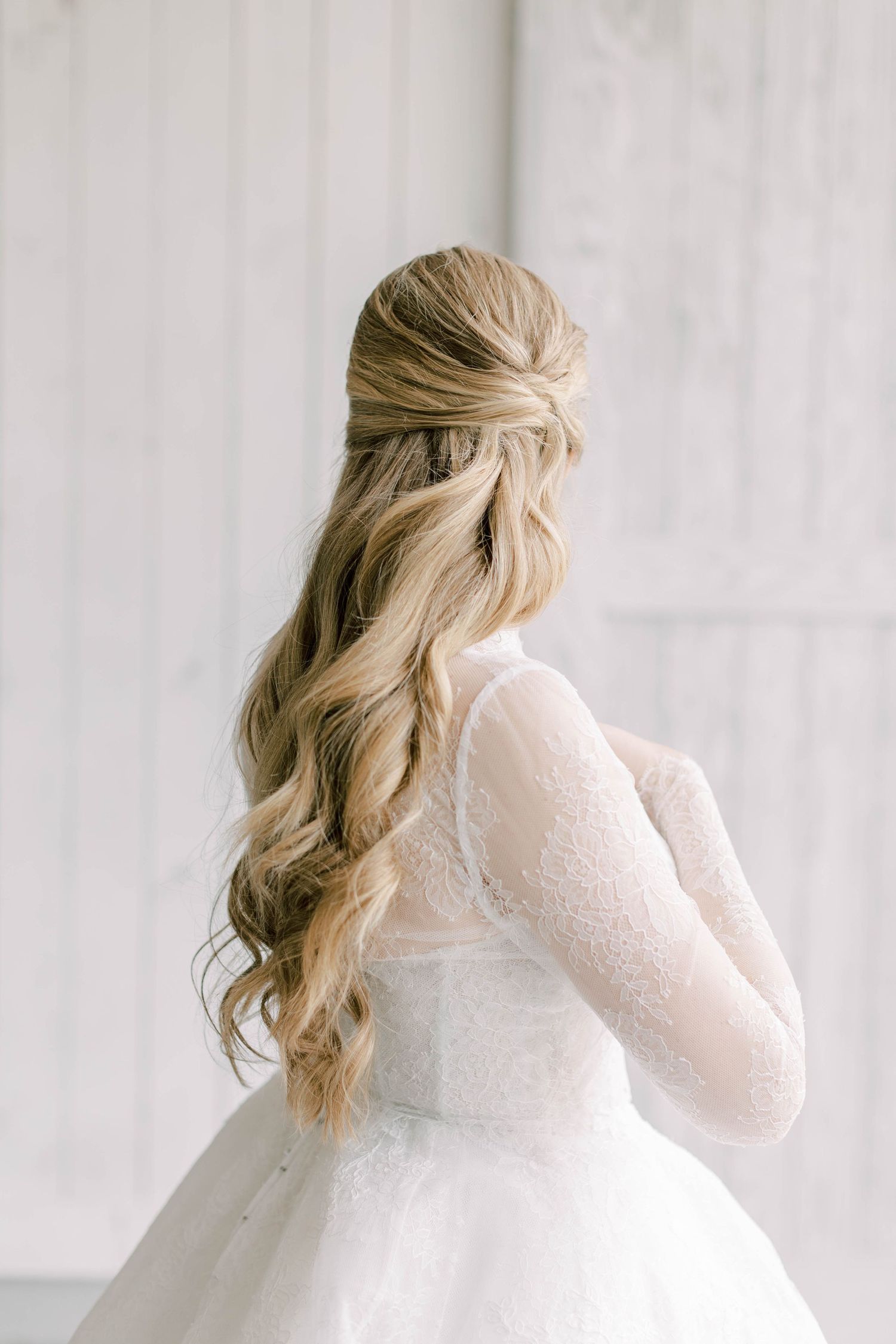 Elegant bridal hairstyle featuring long blonde waves and half-up styling.
