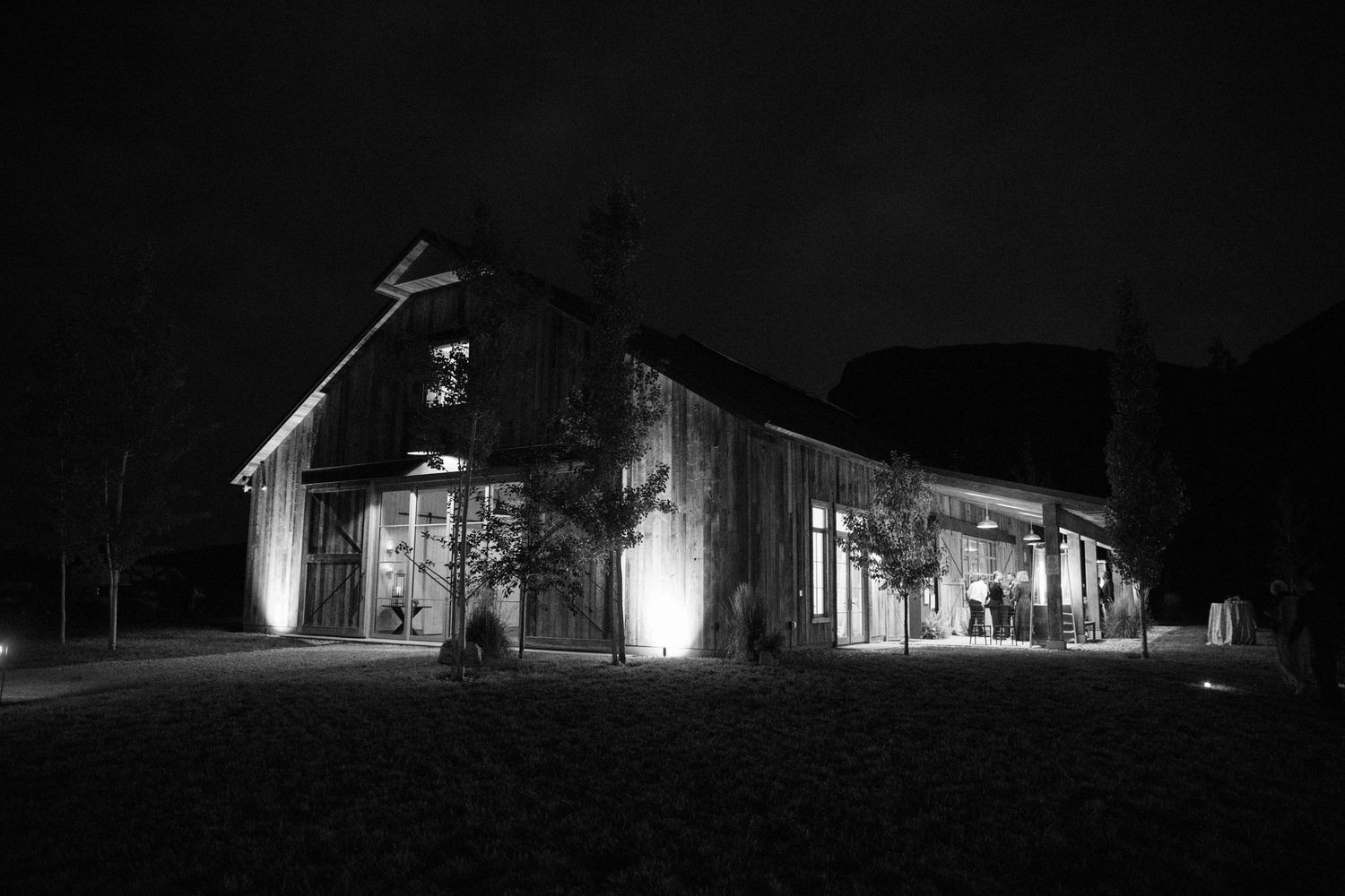 Black and white photo of an illuminated barn venue at night during a wedding reception.