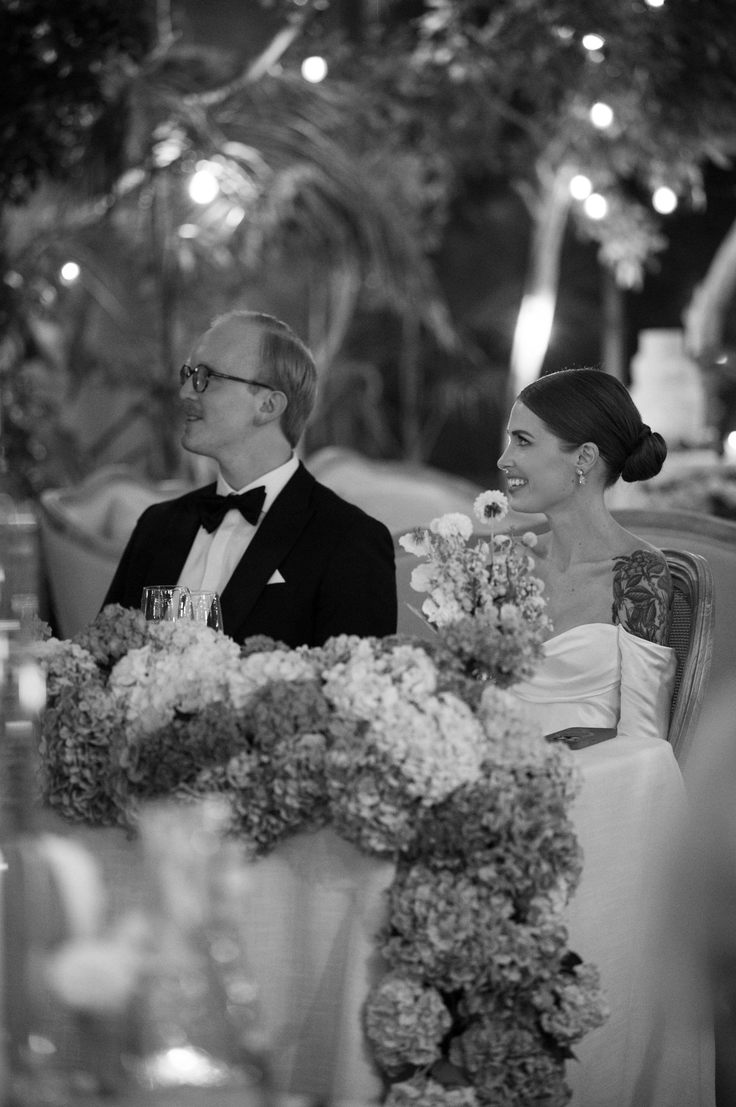 Black and white photo of formal dinner with elegant hydrangea centerpieces and twinkling lights.
