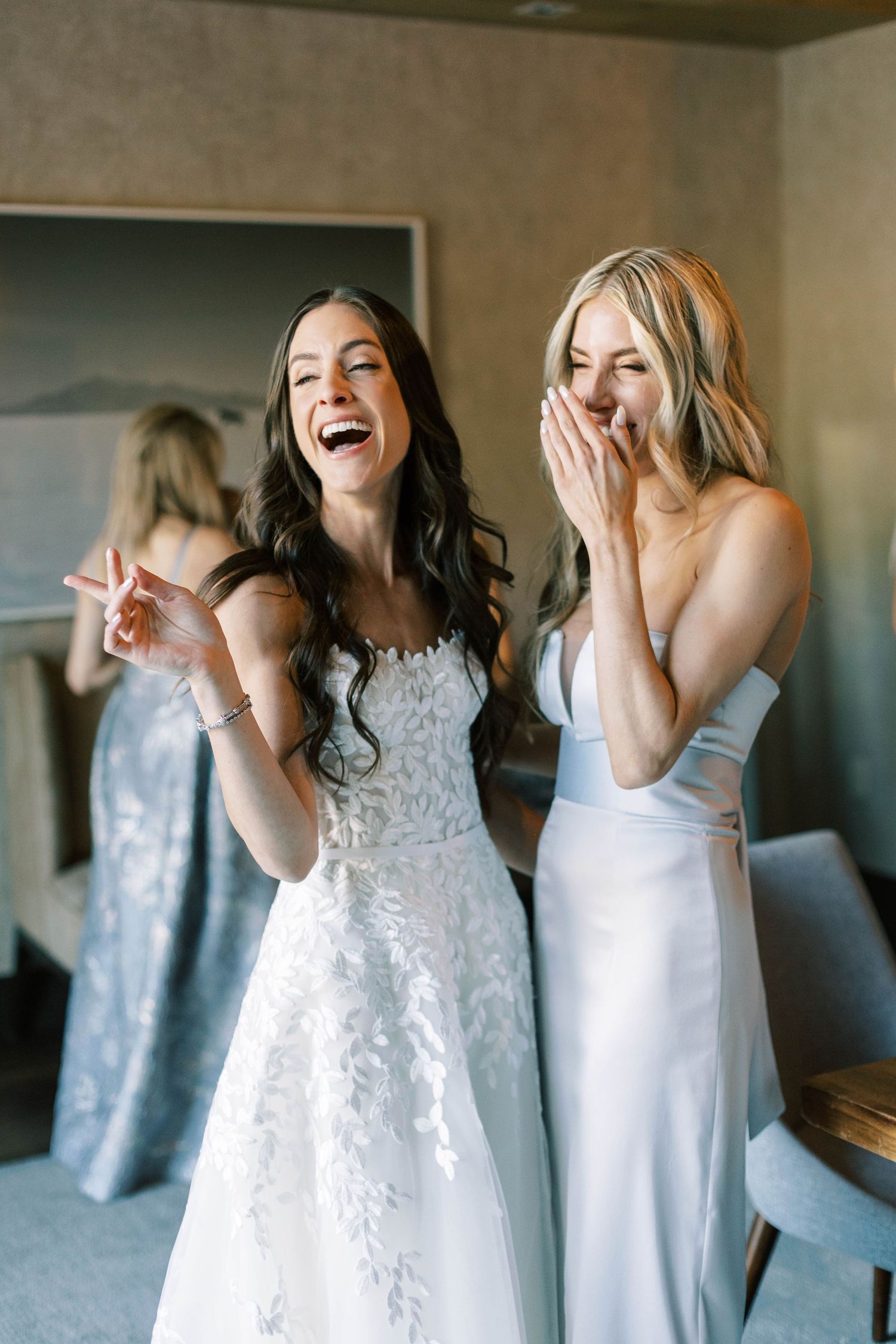 Two women in white dresses share a joyful laughing moment together.