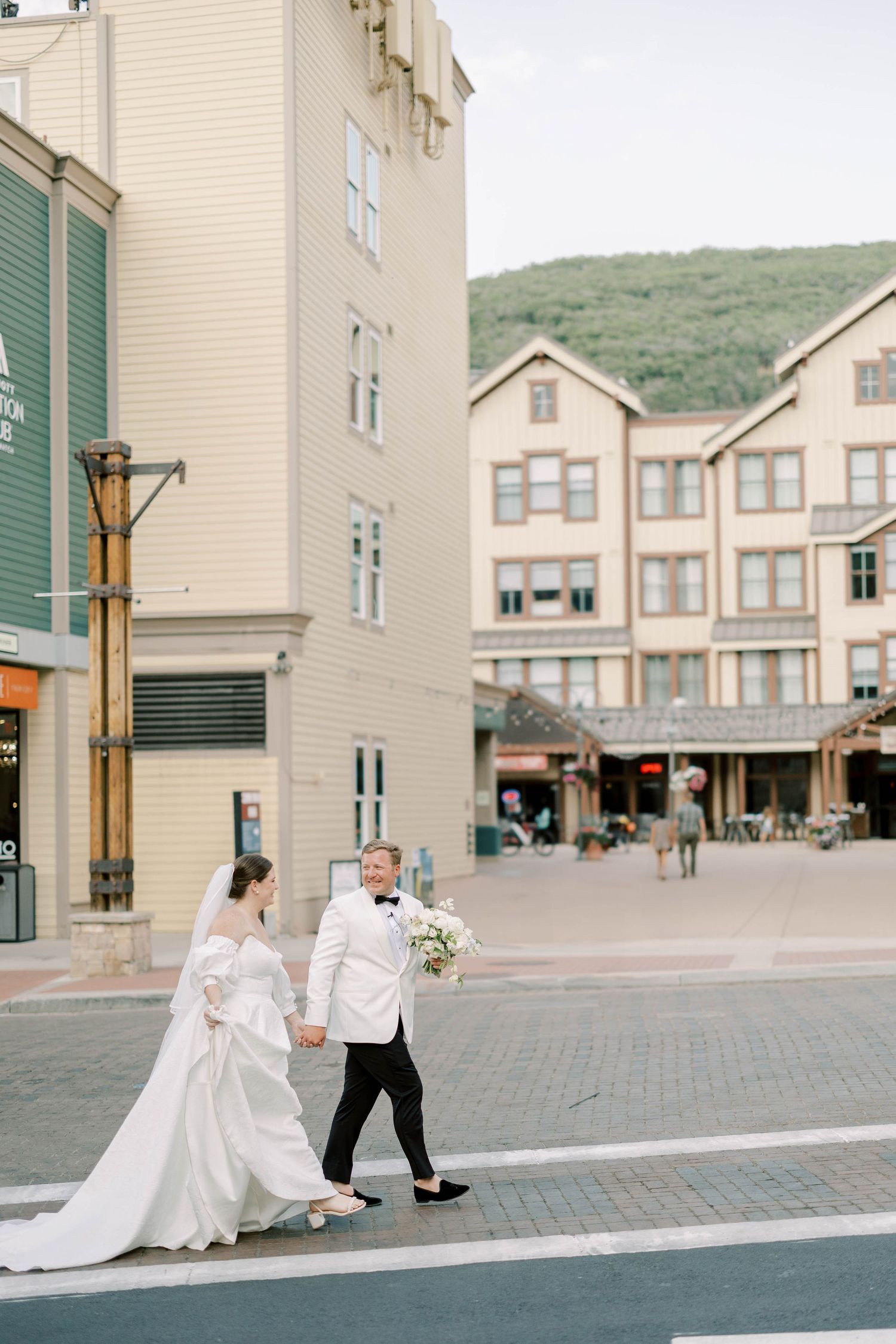 Couple walking together through city streets of Park city on their wedding day with mountain backdrop.